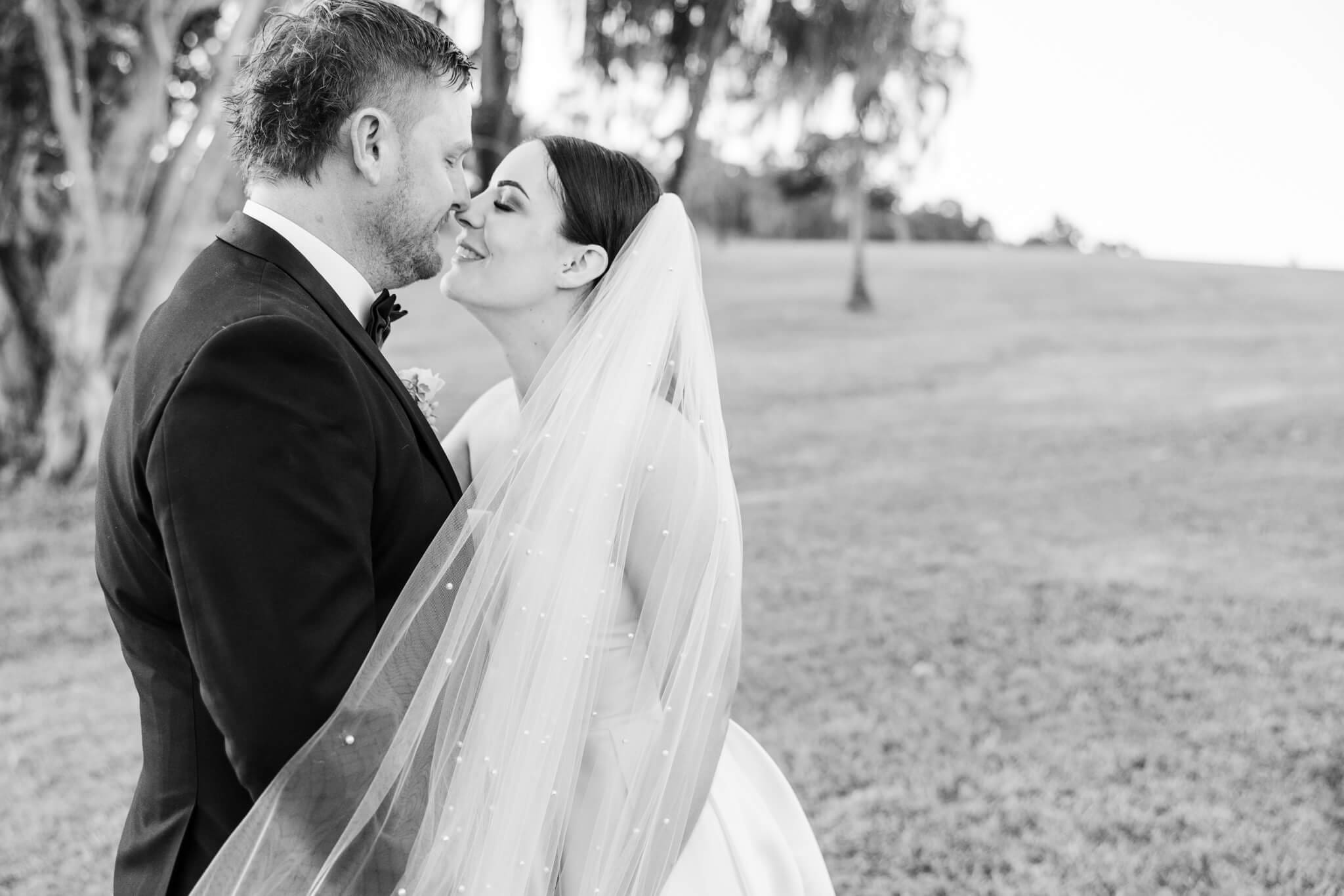 Black and white image of the bride and groom leaning towards each other for a kiss.