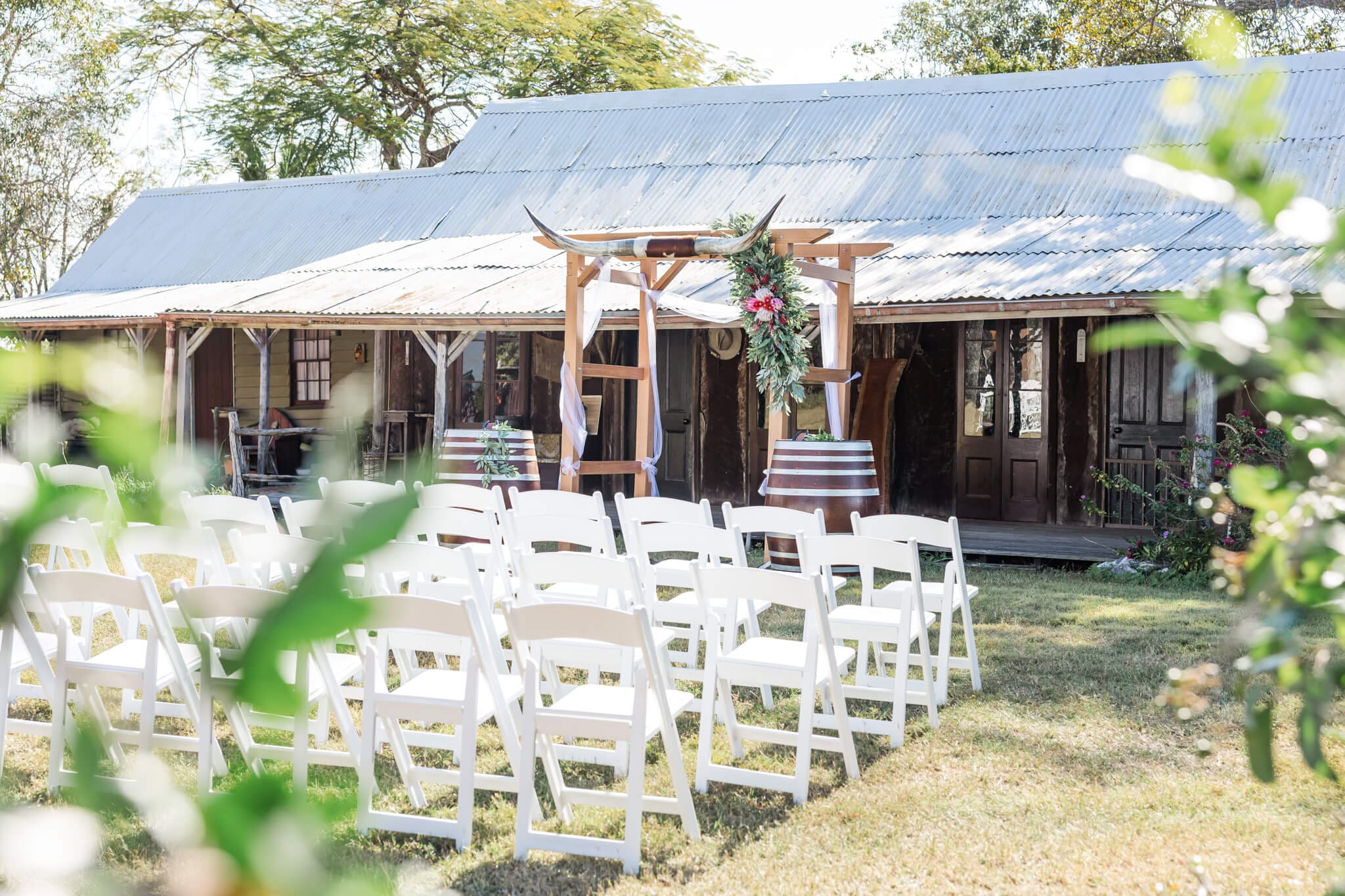 Wedding ceremony set up at Glenmore Homestead Rockhampton with a wedding arbor, white guest chairs and two barrels to emphasize the rustic look.