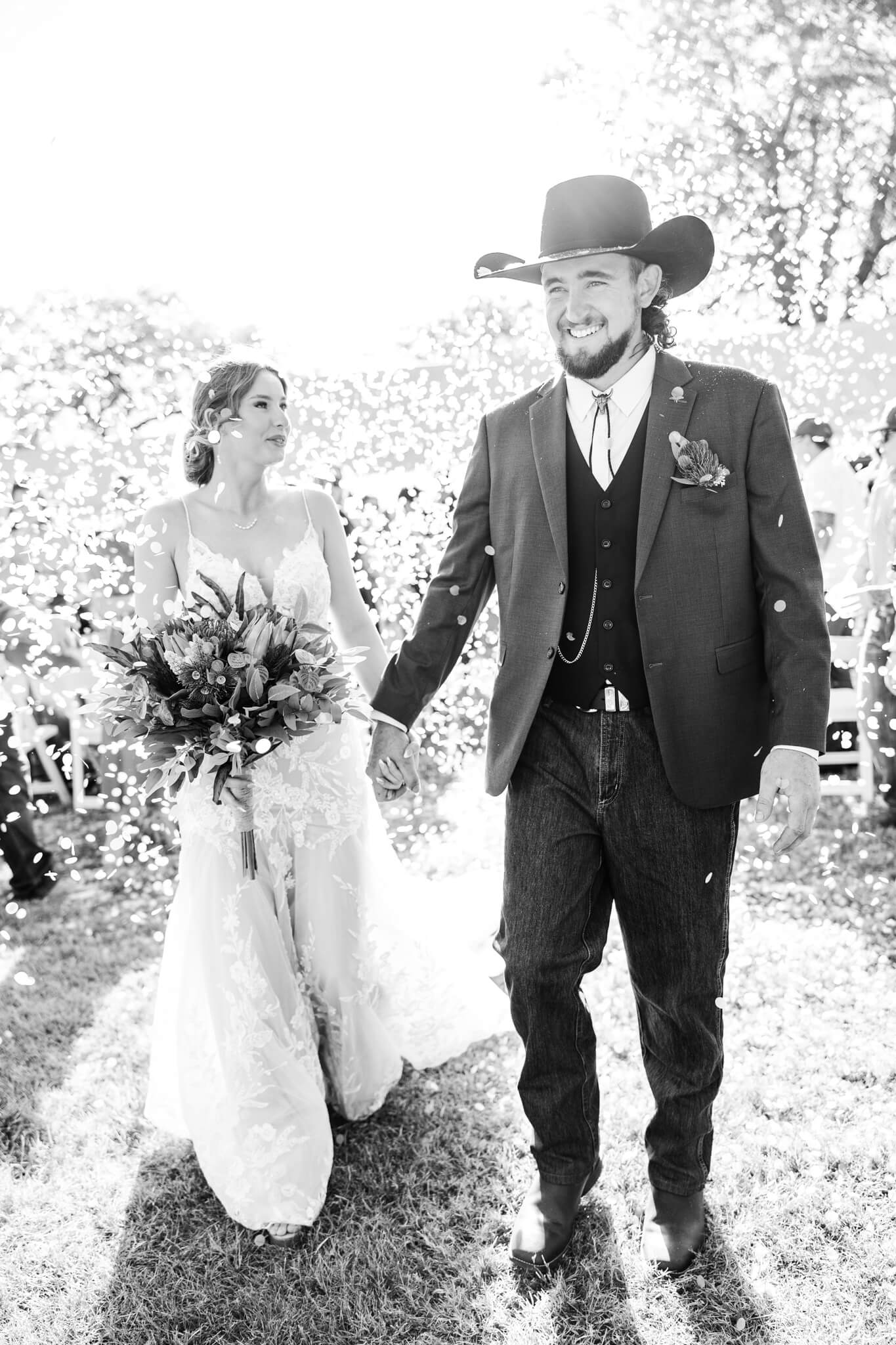 Black and white image of a couple emerging from a huge cloud of confetti as they walked back down the aisle.