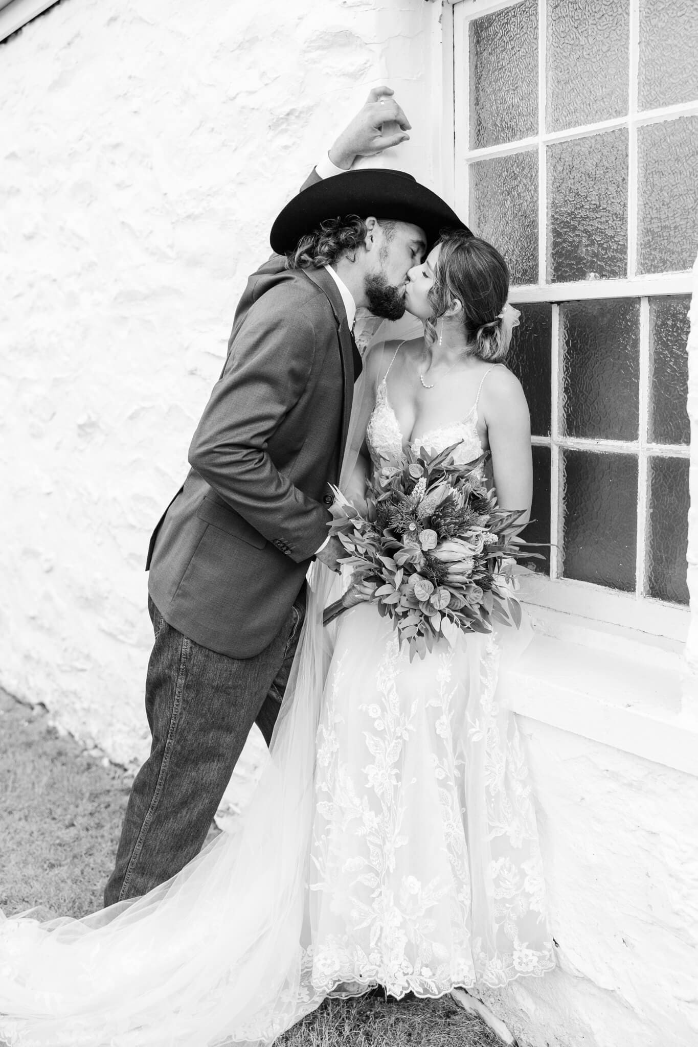 Bride and groom share a kiss as the bride sits on an outside window ledge at the Glenmore Homestead Rockhampton. 