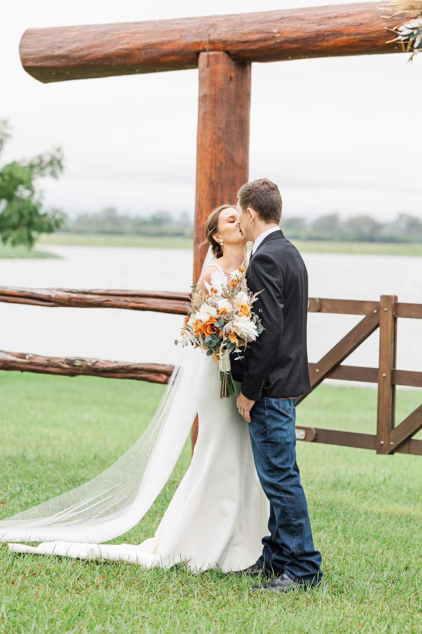 Bride and Groom seal a their marriage vows with a kiss near a set of yard gates and rails at one of the Rockhampton wedding venues, Queensland.