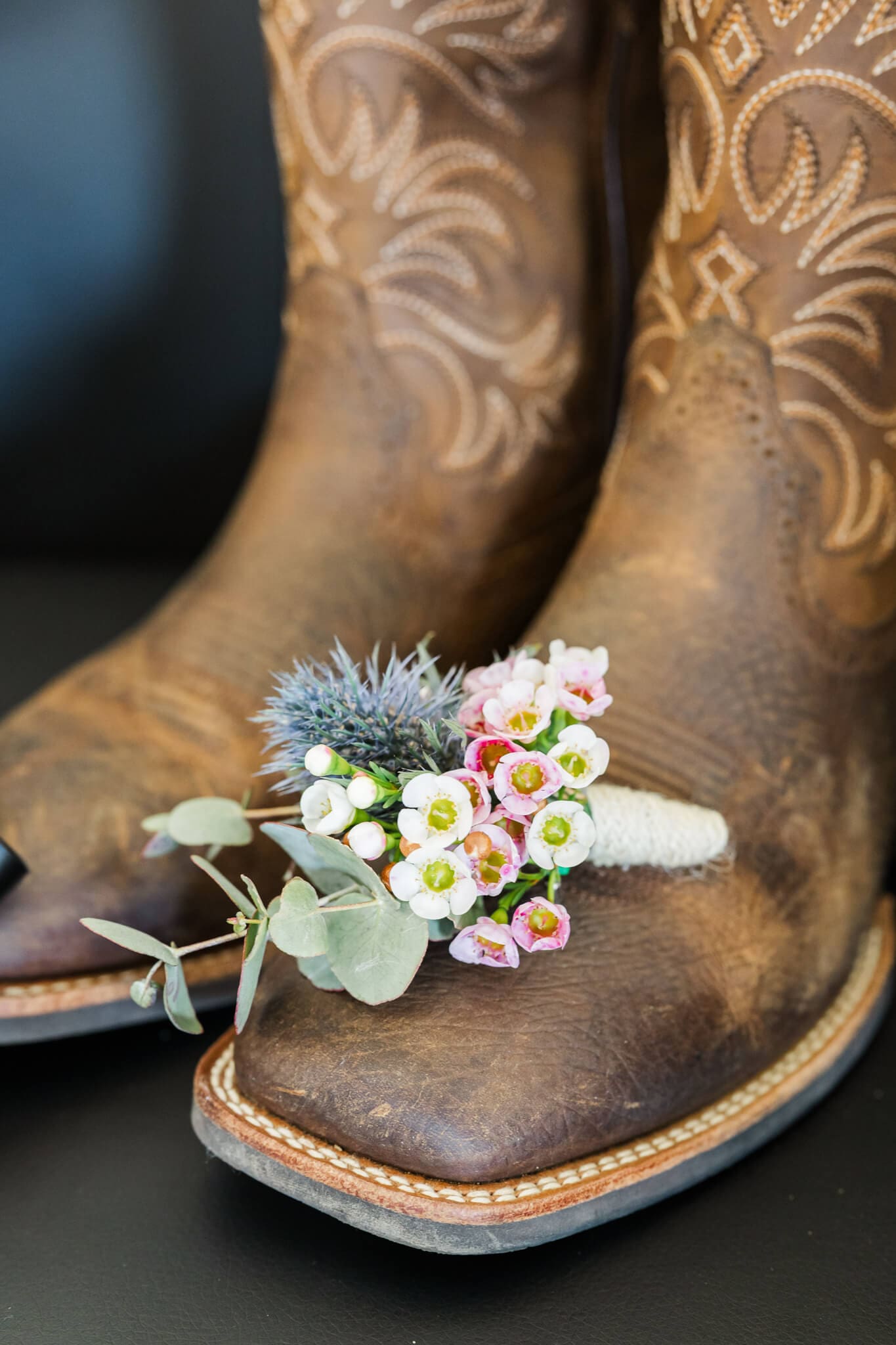Detail shot of a groom's boutonniere on his brown western cowboy boots.