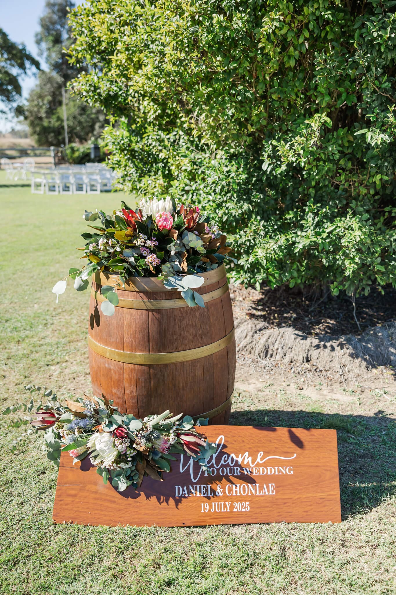 Detail shot of the styling at a wedding featuring a rustic barrel, native flowers and a wooden sign welcoming you to the wedding.