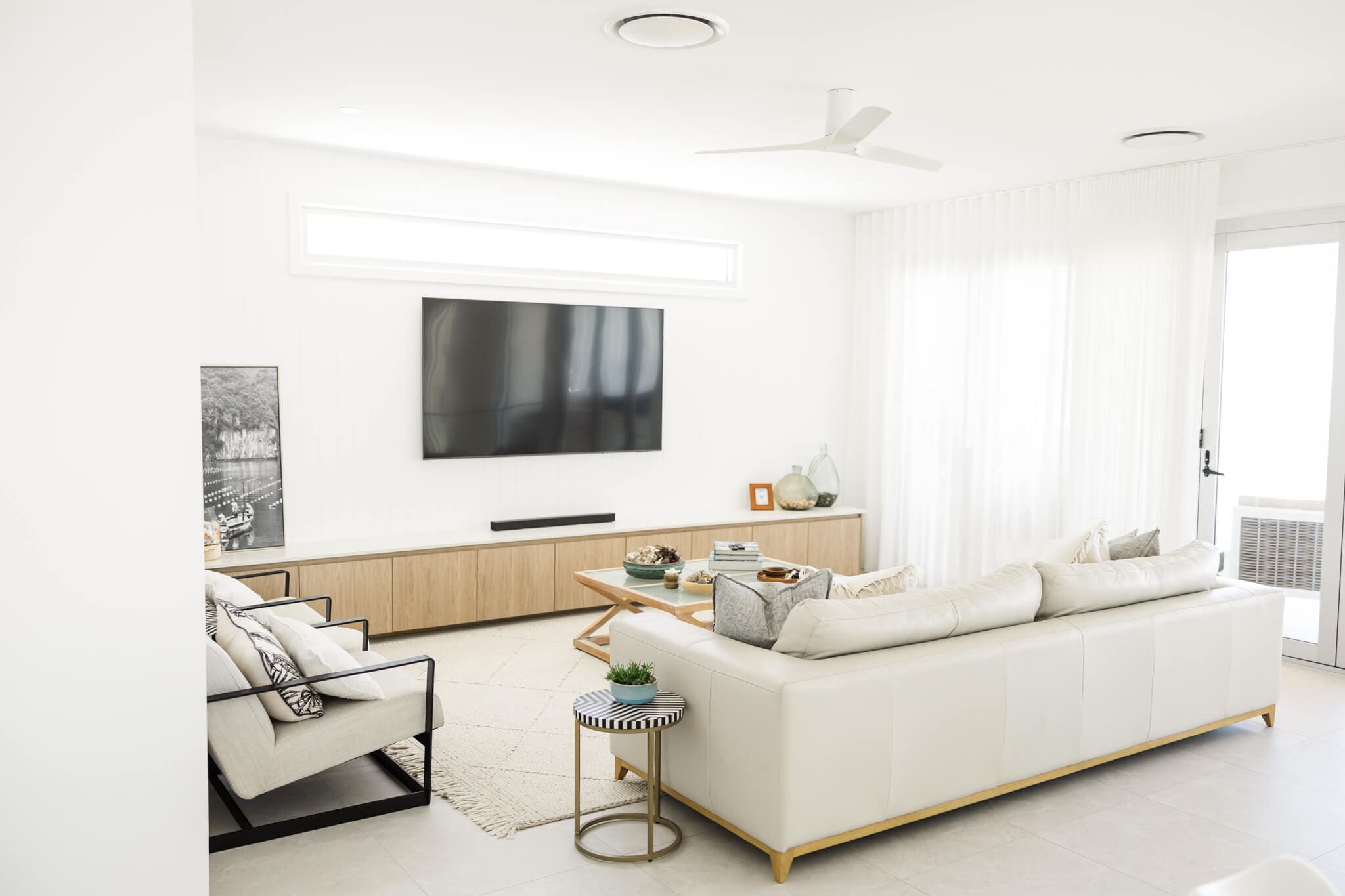 Living area including a cream coloured lounge suite, a large flat screen monitor and decor. Captured by Airbnb photographer Julie-Anne Photography.