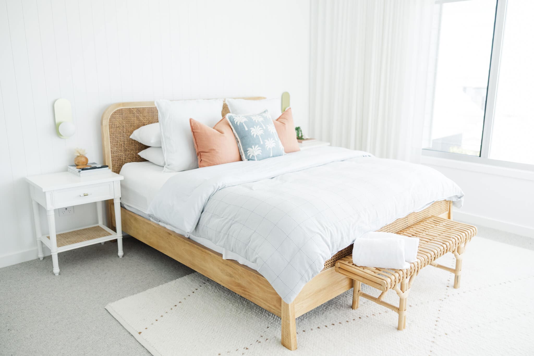 A beautifully styled bedroom with a queen bed, light wooden bed frame, white quilt and blue and pink cushions. Captured by Airbnb photographer, Julie-Anne Photography