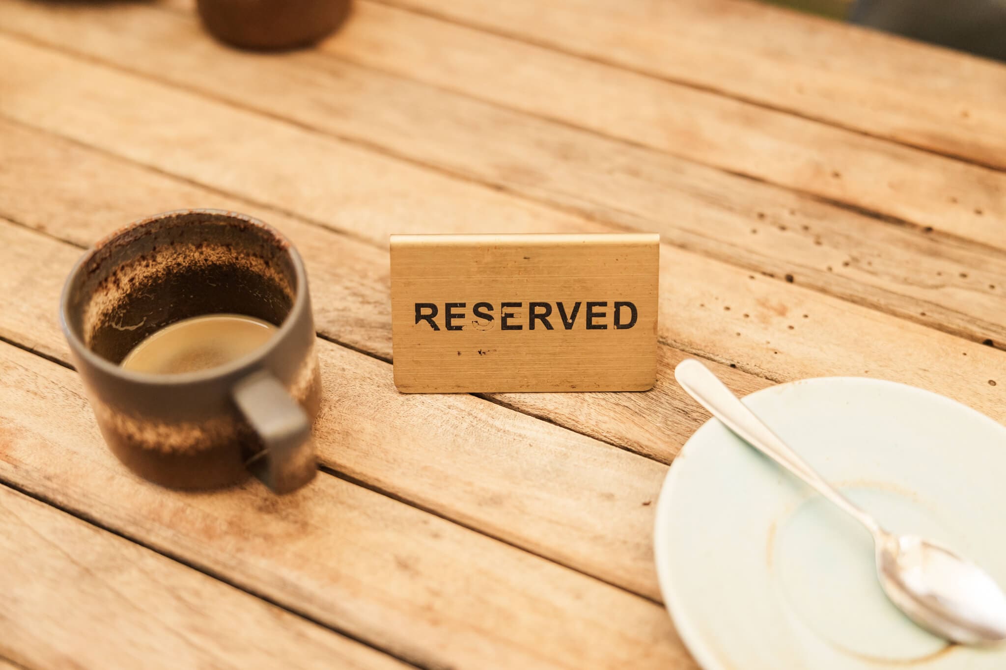A coffee cup,, reserved sign and an empty plate sitting on a wooden table.