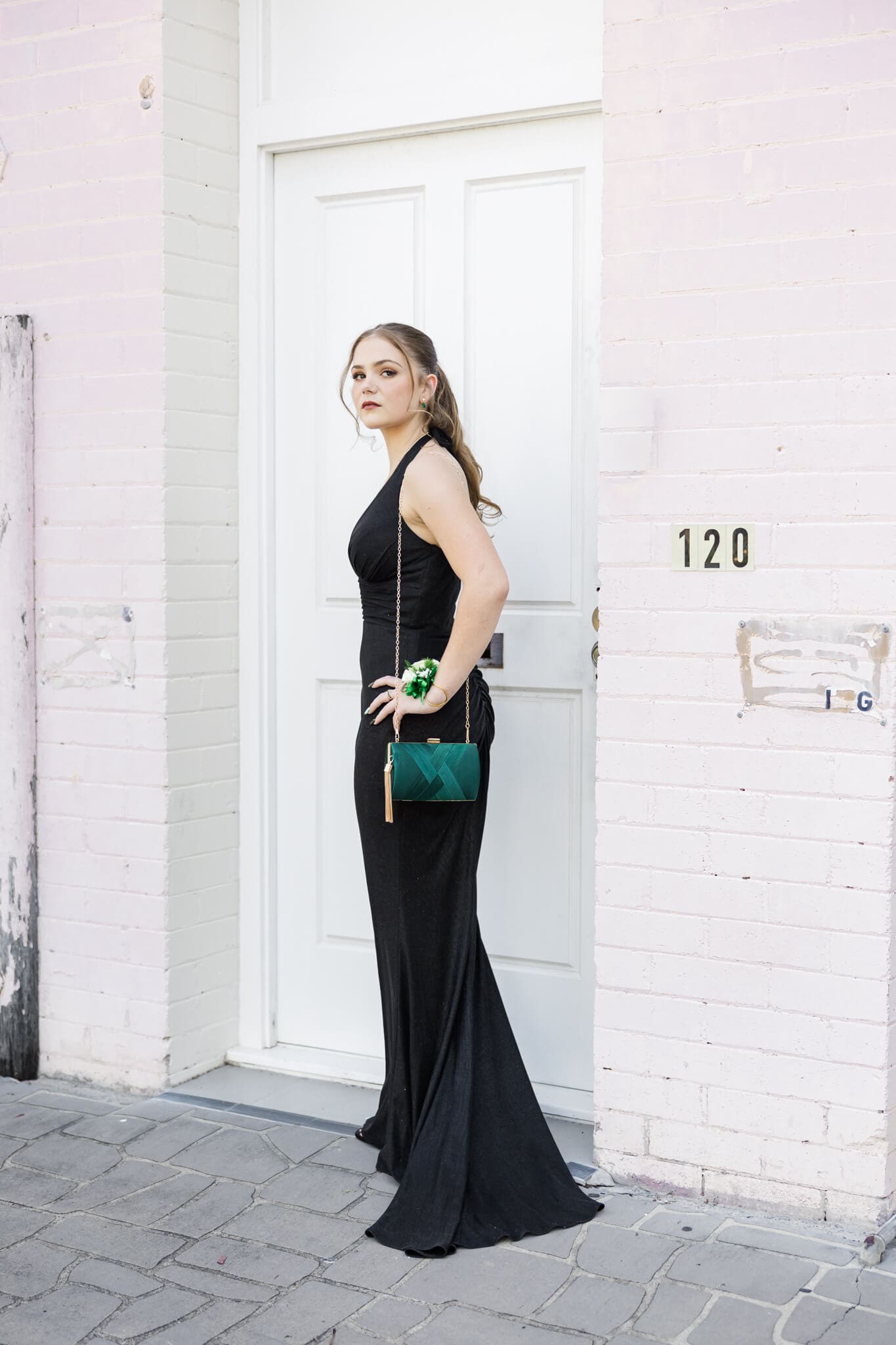 Formal graduate session with a girl posing near a pink and white door area.