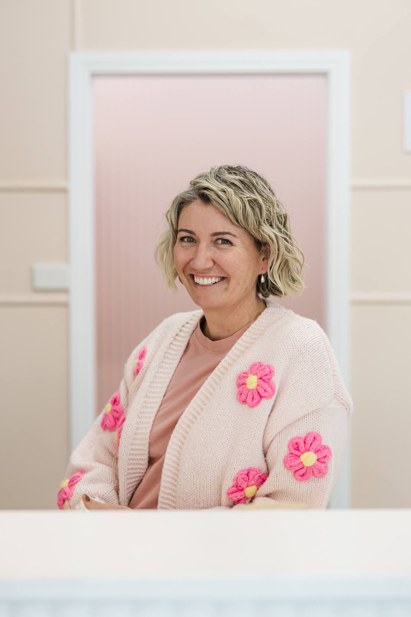 Florist poses for a headshot dressed in a pink top with pink flowers in front of a pink background.