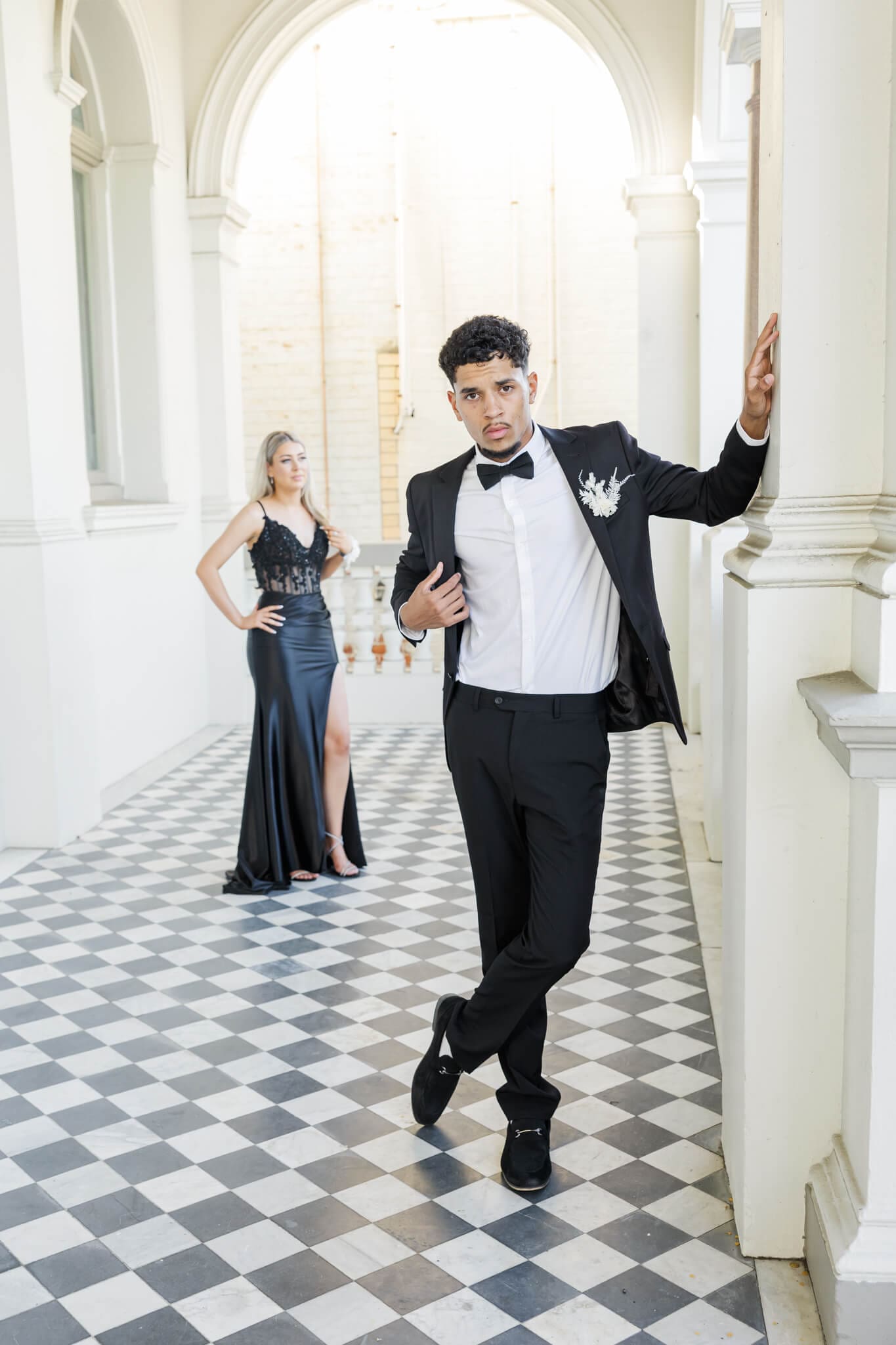 Graduates poses for their formal session in a beautiful cream building with a black checkered floor.