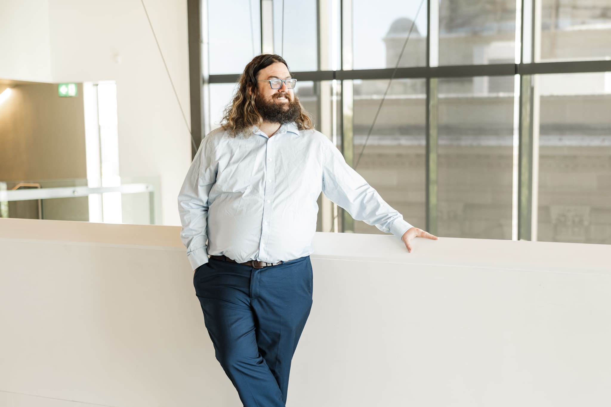 Wedding Celebrant, Married by Mitchell, stands by a cream wall, looking out to the distance.