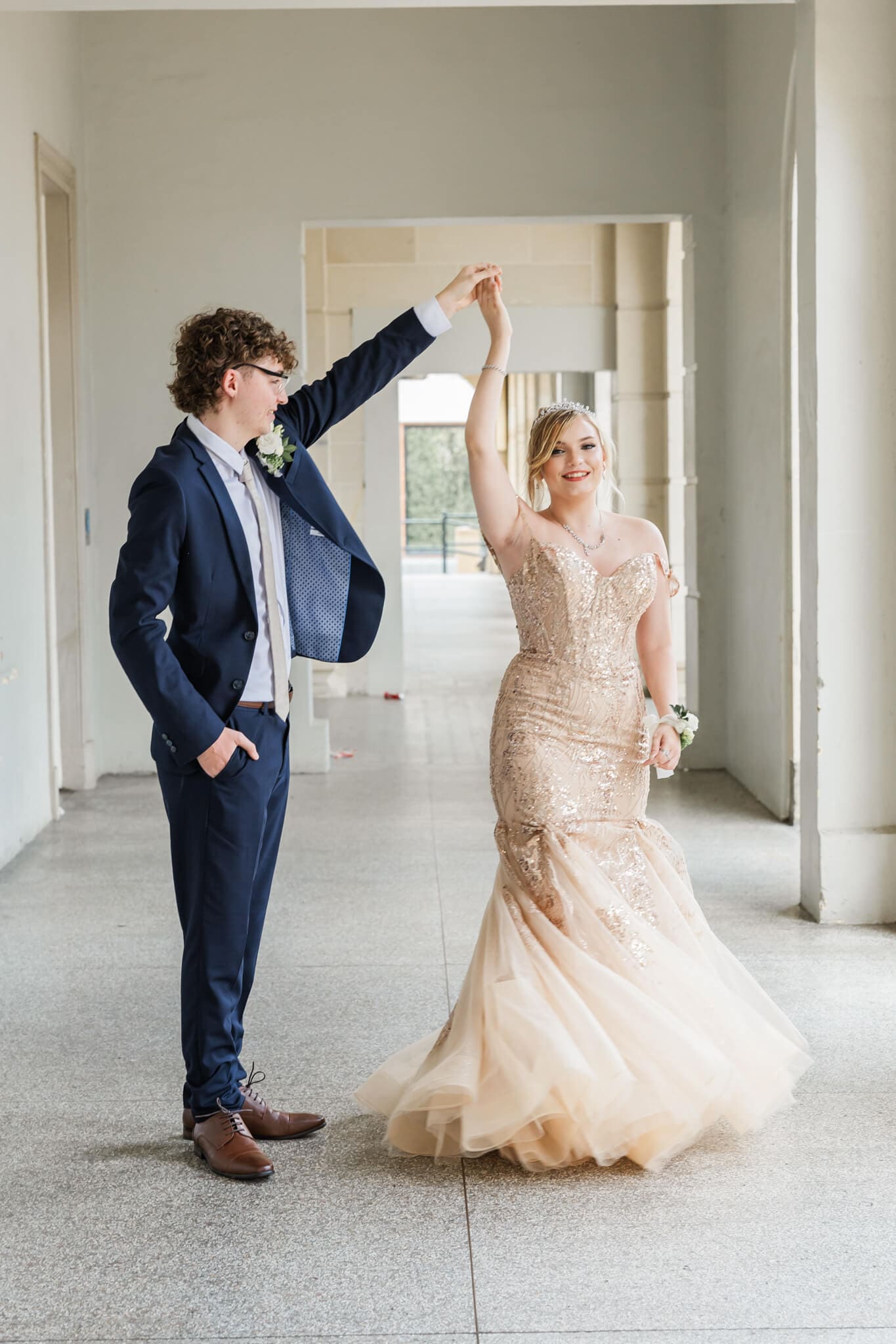 Two graduates pose for their formal photography session. Boy twirls the girl in her formal dress.