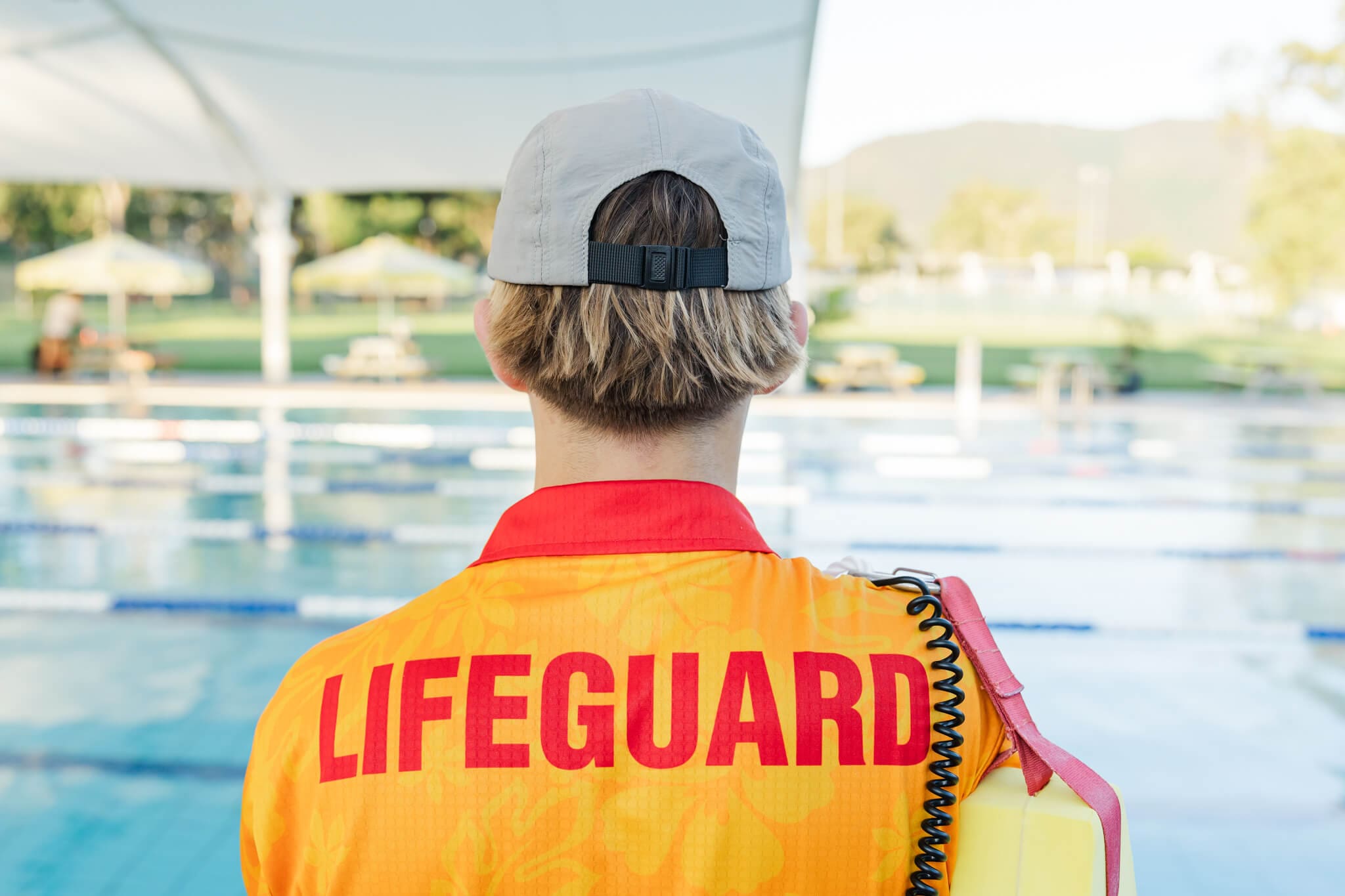 Lifeguard on duty in a bright orange shirt, near a swimming pool.