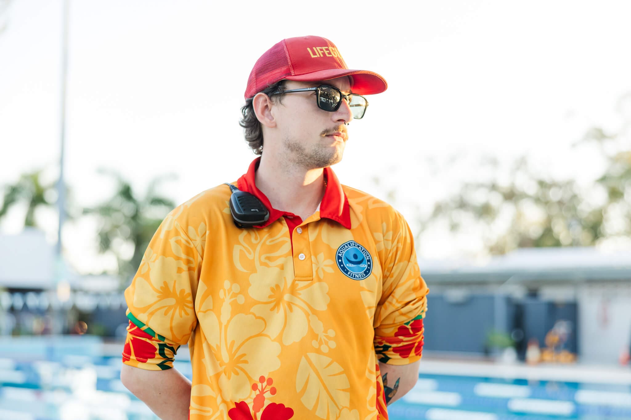Lifeguard in a bright orange shirt, standing near a pool on duty.