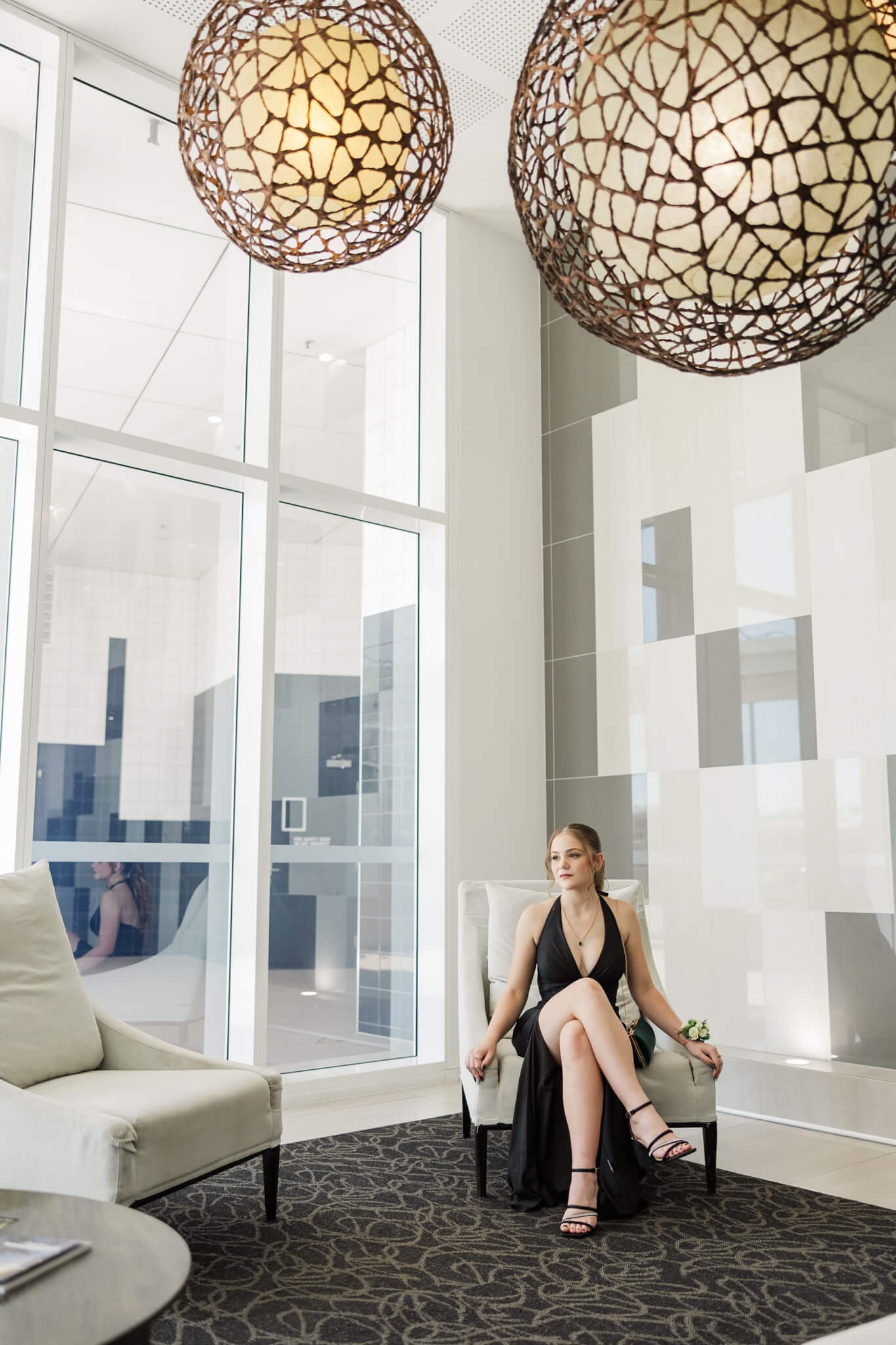 Gorgeous school formal photo of a girl in her black gown, seated looking out a large window wall. Captured by Rockhampton Formal Photographer, Julie-Anne Photography