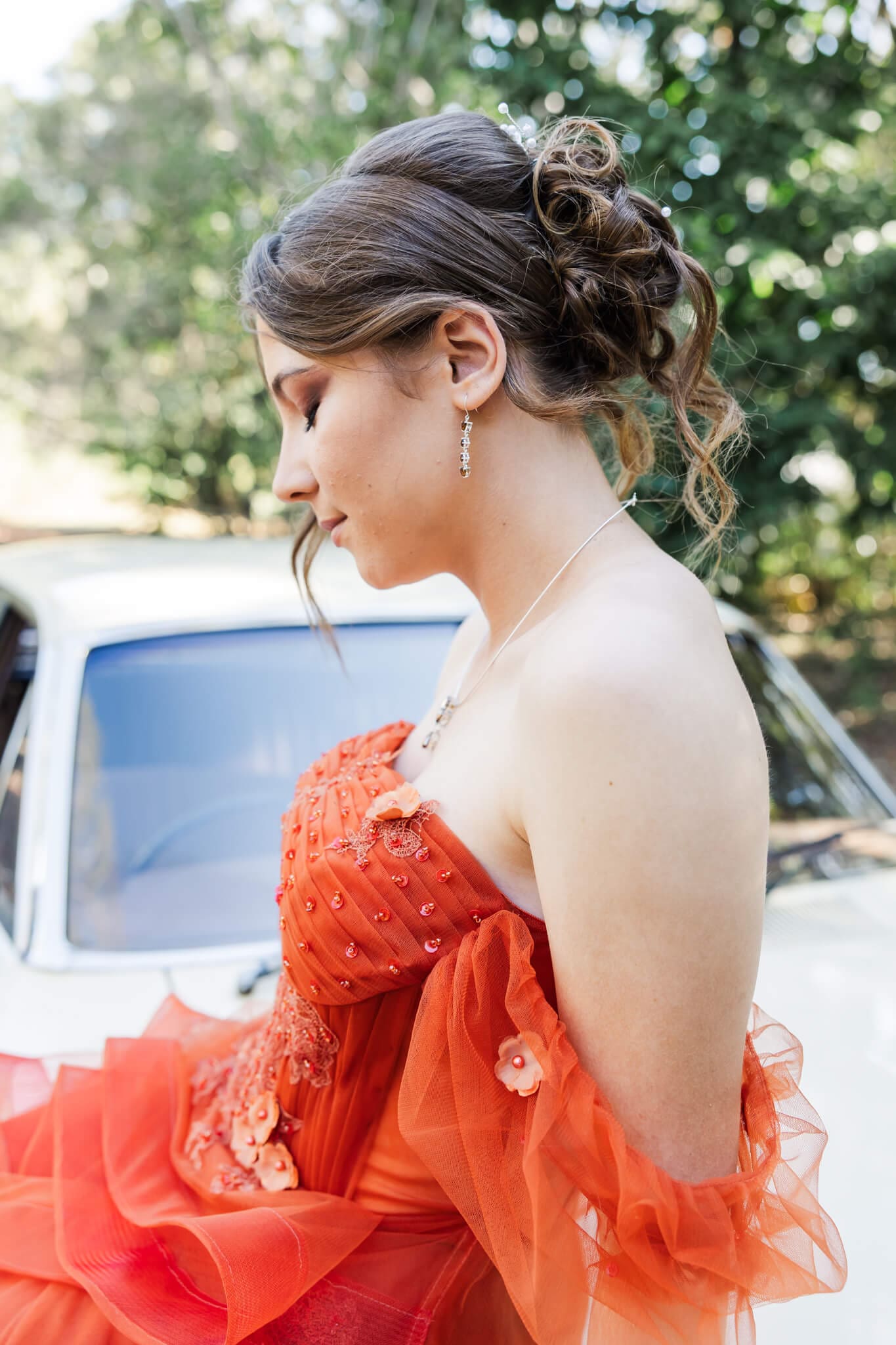 Girl in an burnt orange dress seated on a bonnet of an old car.