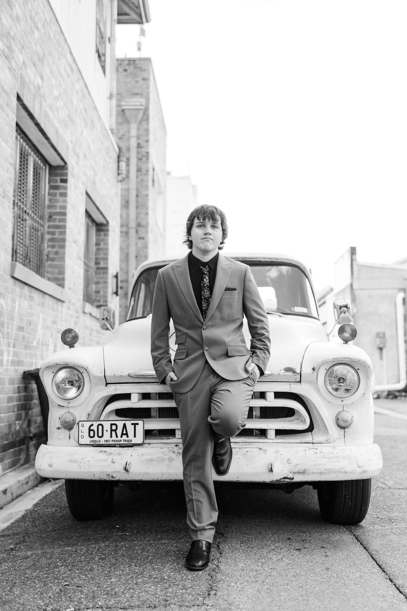 Black and white image of a high school senior posing for his school formal photos in front of an old holden ute.
