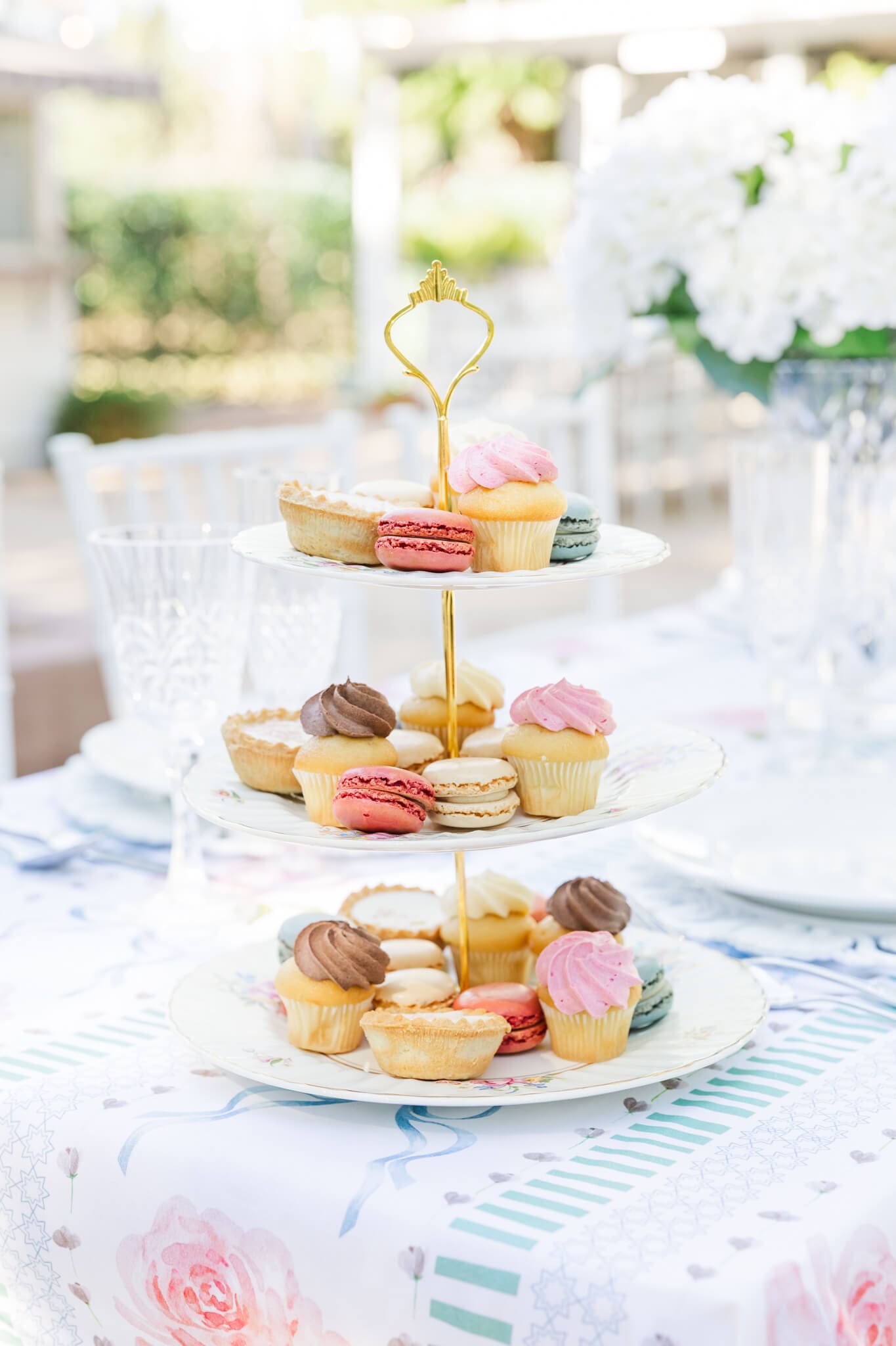 a three tier cake stand filled with colourful cakes, muffins and eclairs, giving old English vibes.