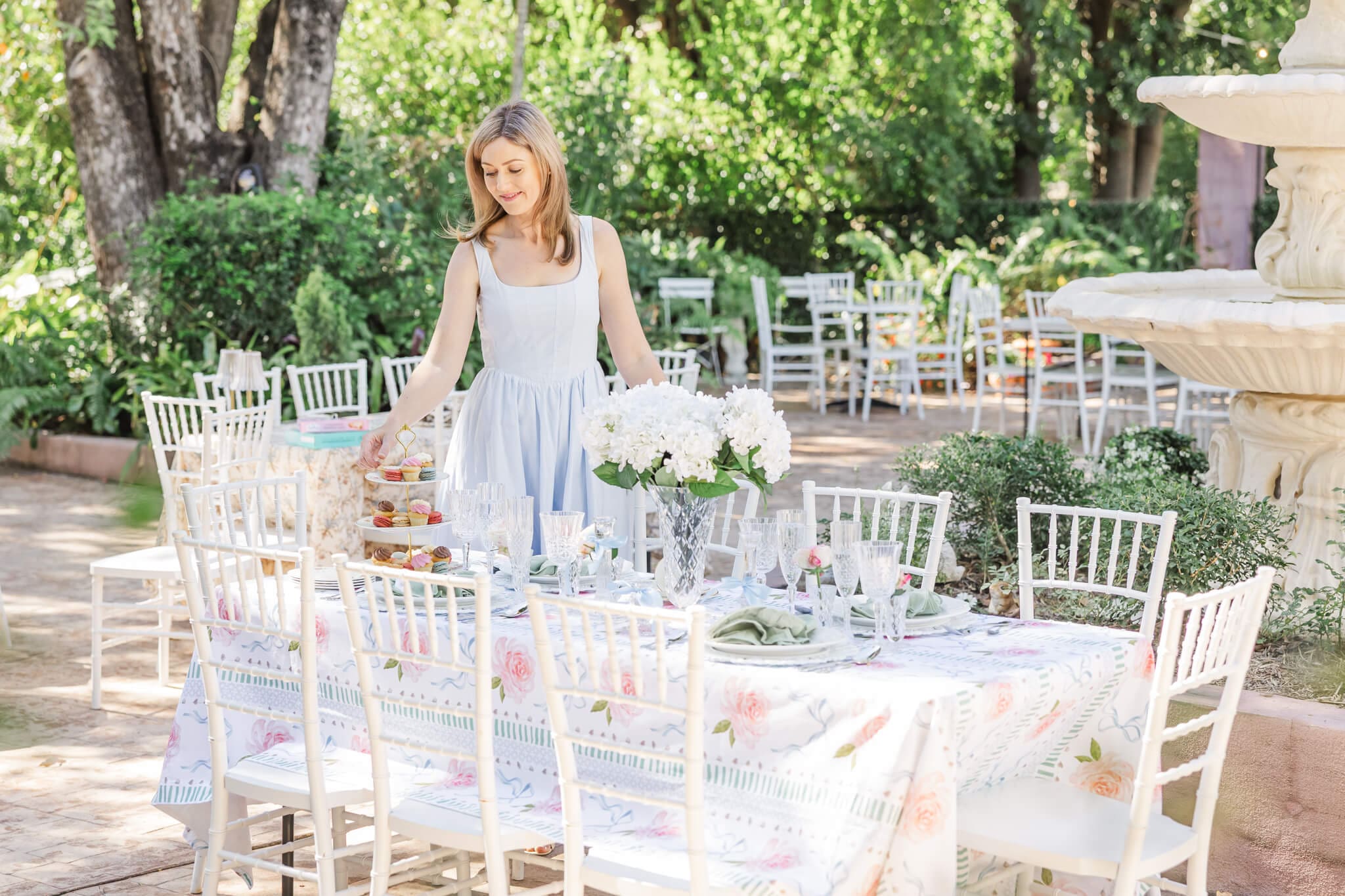 A woman dressed in a blue dress stands next to a beautifully set table in a garden. Taken for her website design in Rockhampton.