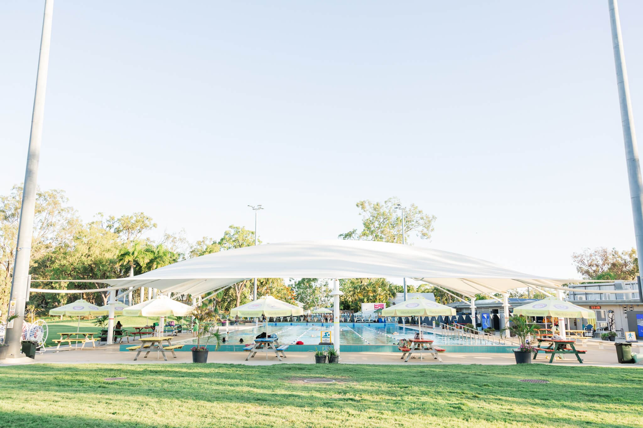 An Olympic sized pool surrounded by a large lawn area with a large cover over half of it.