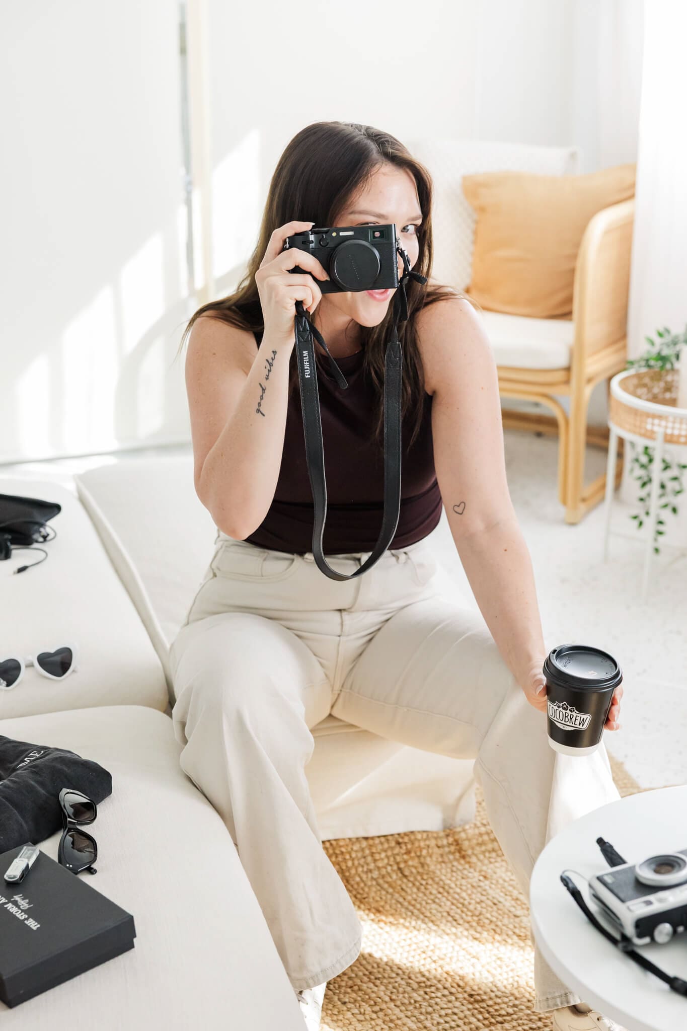 A woman with a camera, holding it up to her face while she poses for a branding session.
