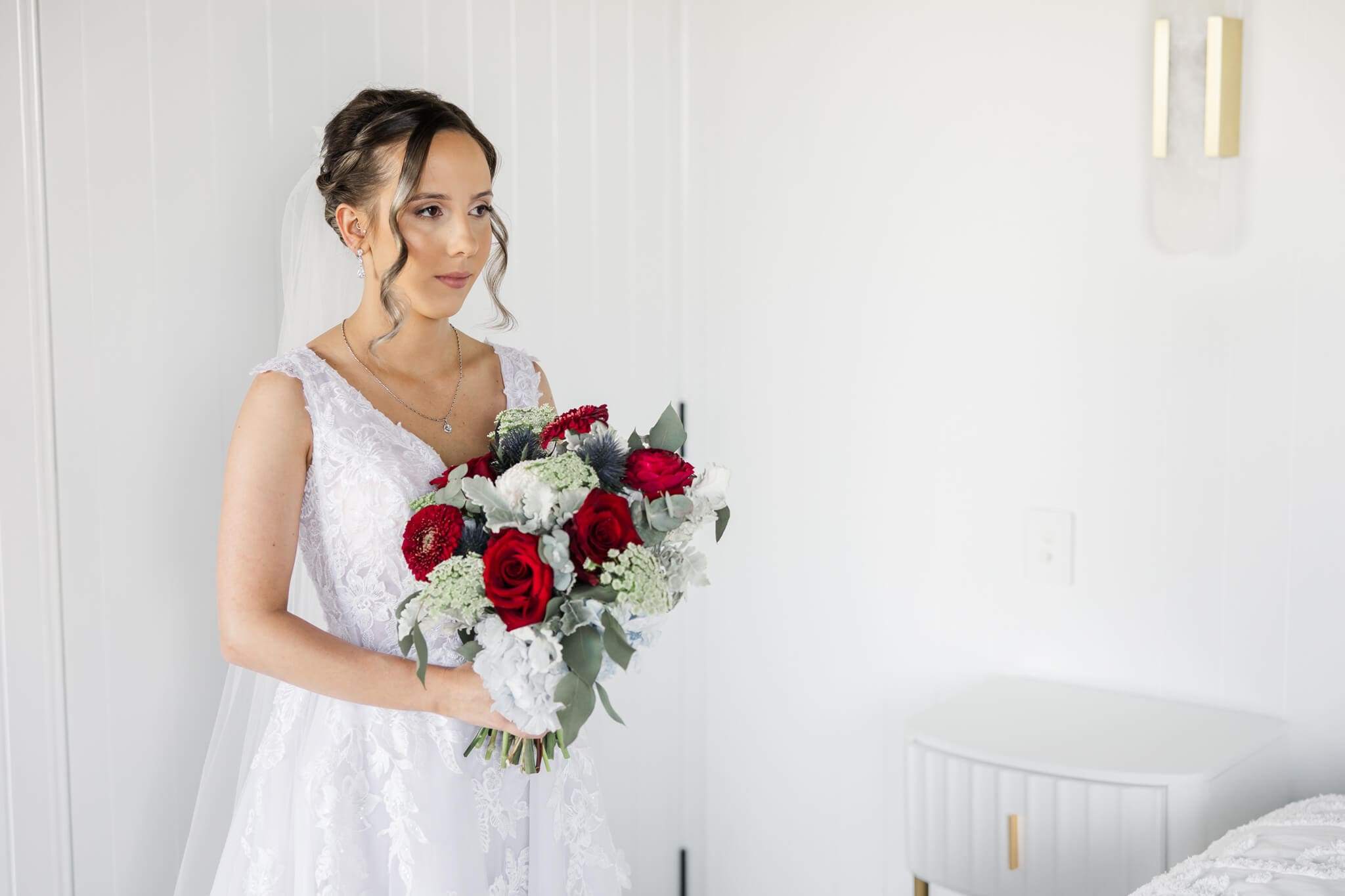 A bride holds her bouquet as she looks wistfully to the side in the bridal suite while wearing her wedding dress.