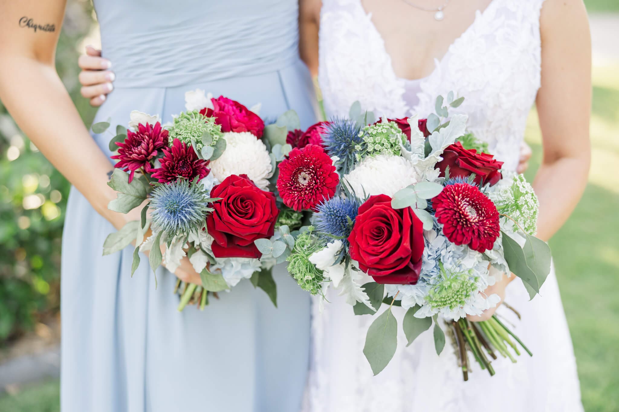 A detail shot of a bride and her maid of honour's bouquets, consisting of red roses and blue flowers against soft muted green tones.