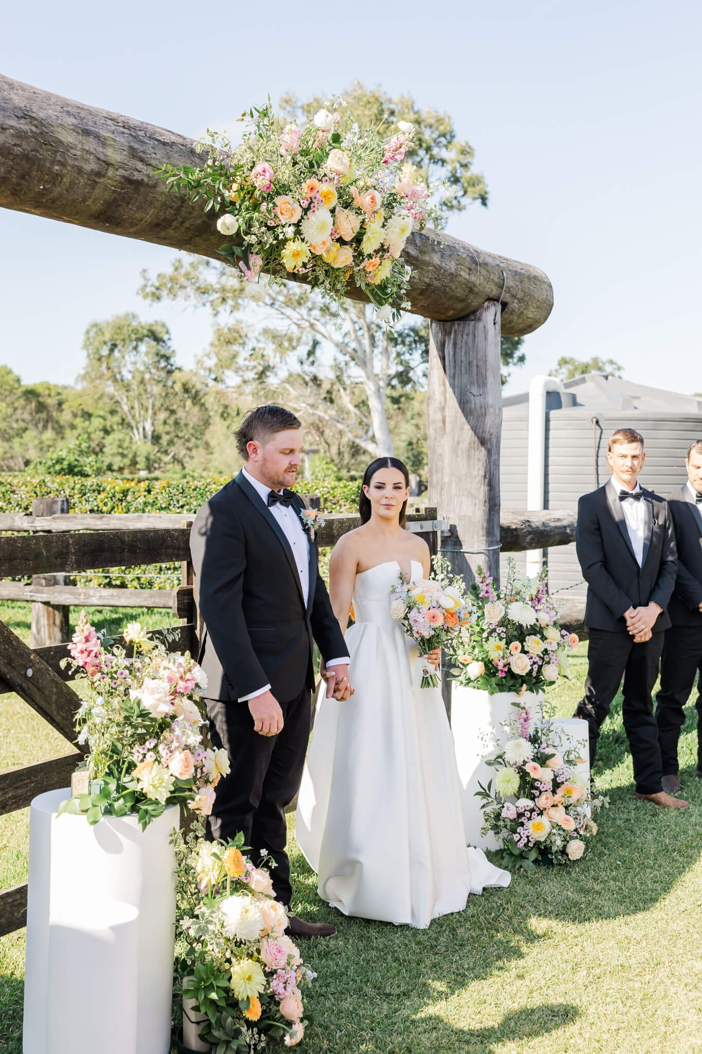 Ceremony site at a Yeppoon wedding venue featuring stunning florals surrounding the bride and groom as they stand side by side, hand in hand.