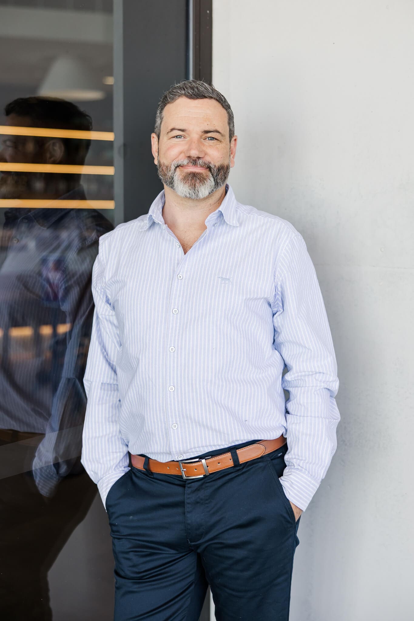 Business man headshot, standing against a cream wall and a black door. Using his photos for marketing in Rockhampton.
