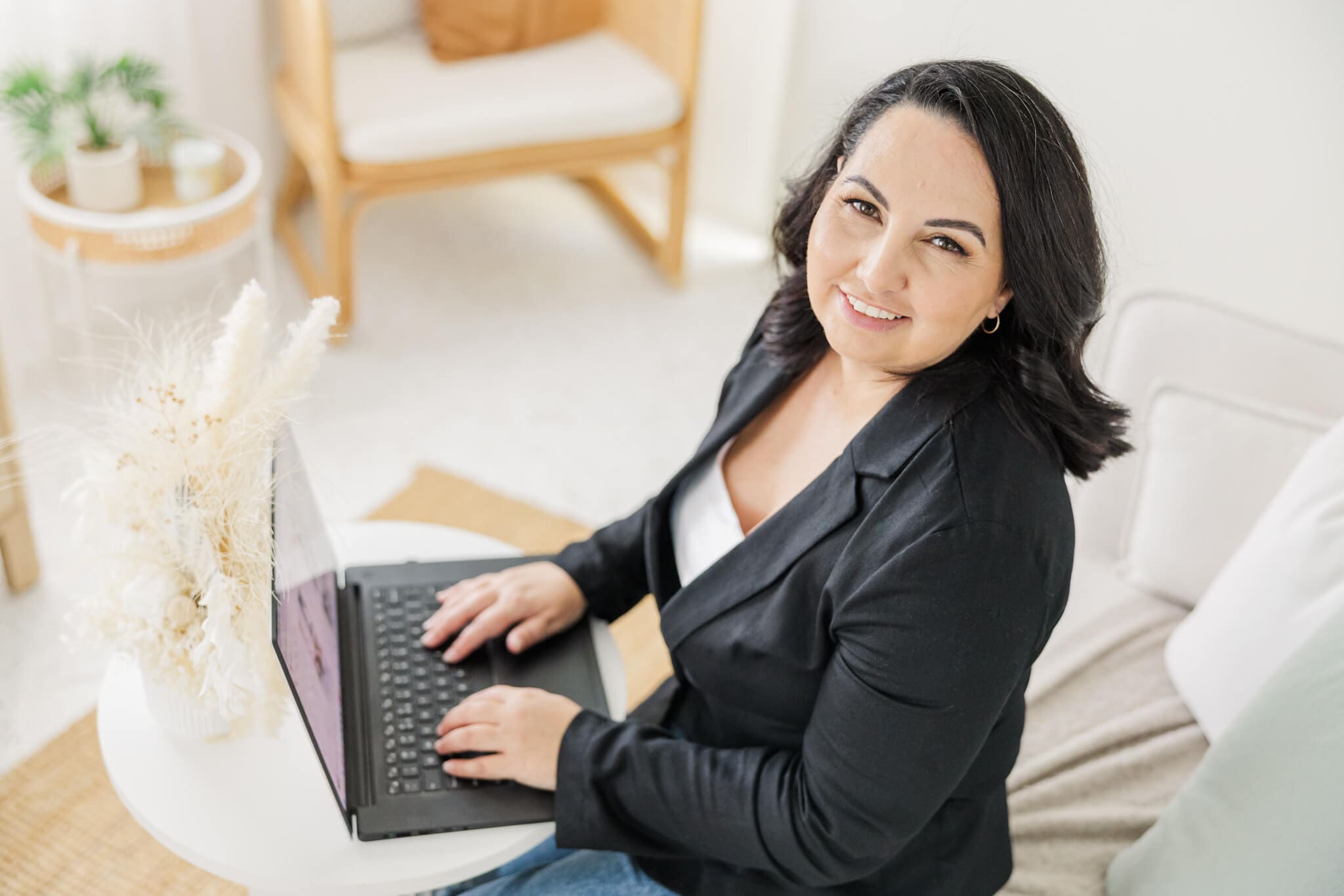 Business woman sits at her laptop, glancing up at the camera. Seated in a cream lounge, posing for photos used for marketing in Rockhampton.