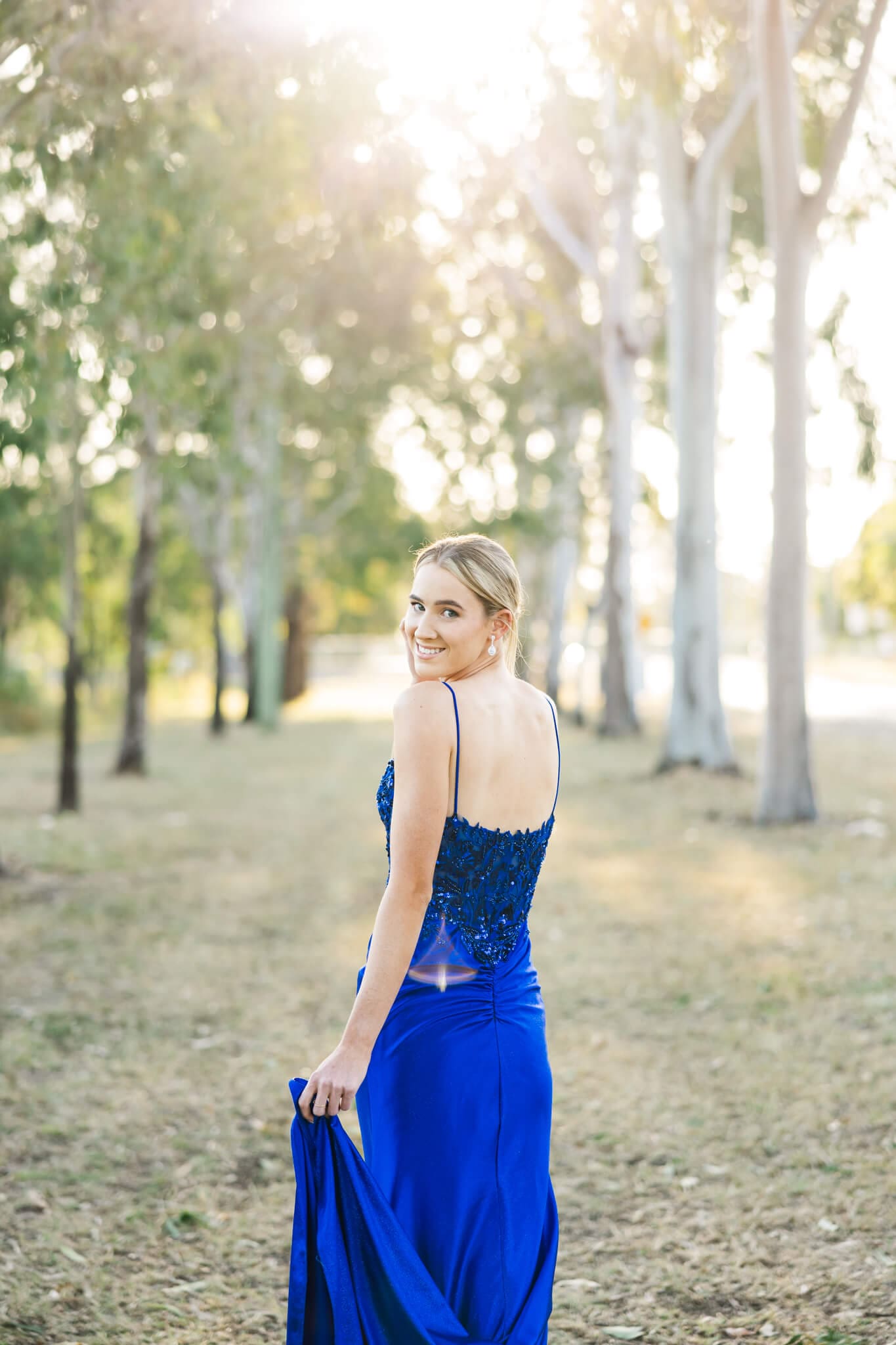 Beautiful graduate dressed in a blue gown, posing against the beautiful golden sun.