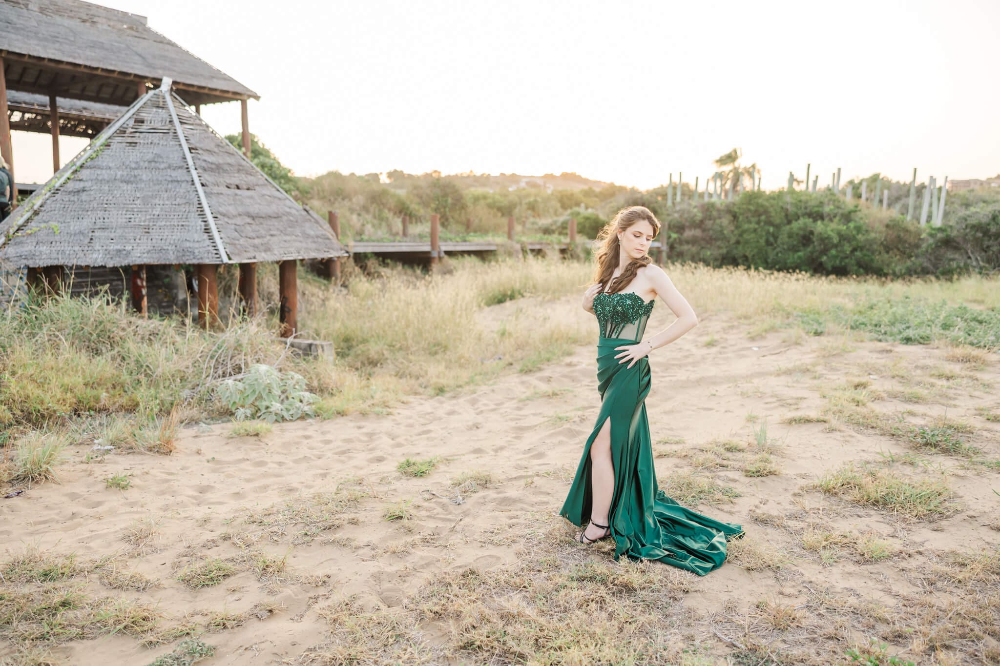 Golden hour photo of a graduate posing in her green gown near some old broken down buildings.