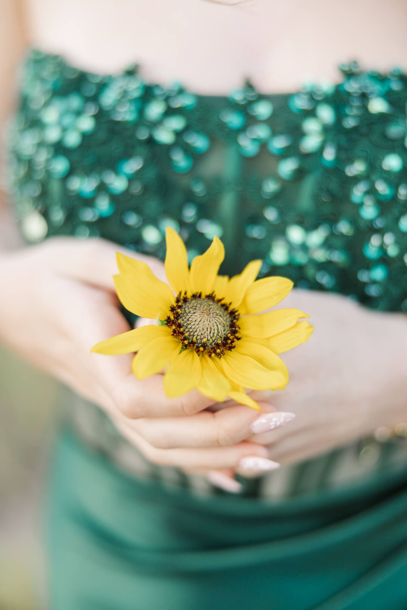Detail shot of a sunflower being held by a girl in a green gown.
