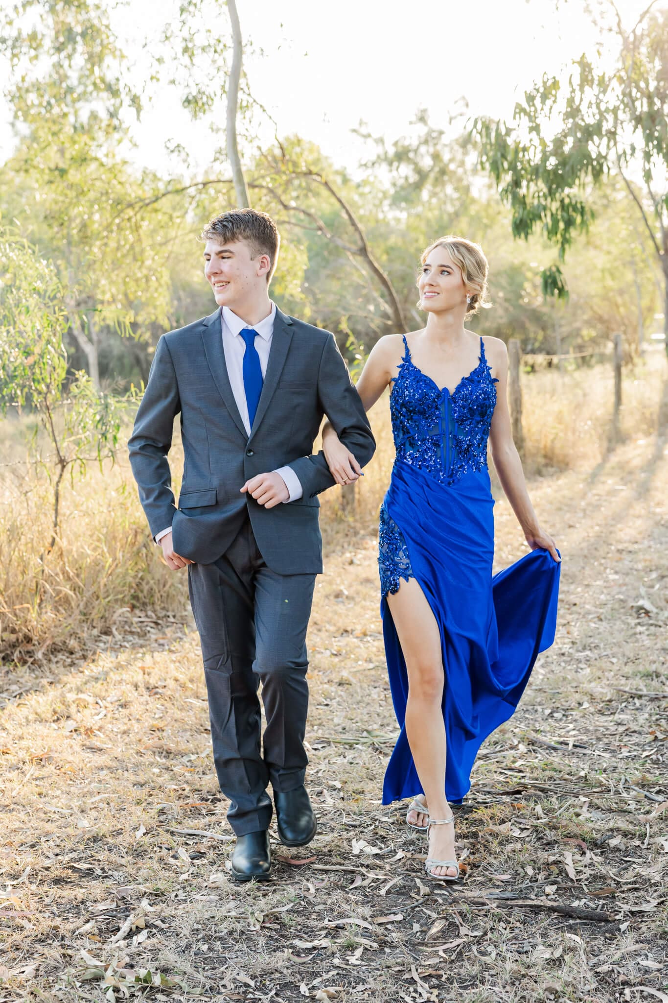 A boy and girl graduate, walking along side a fence during their formal session.