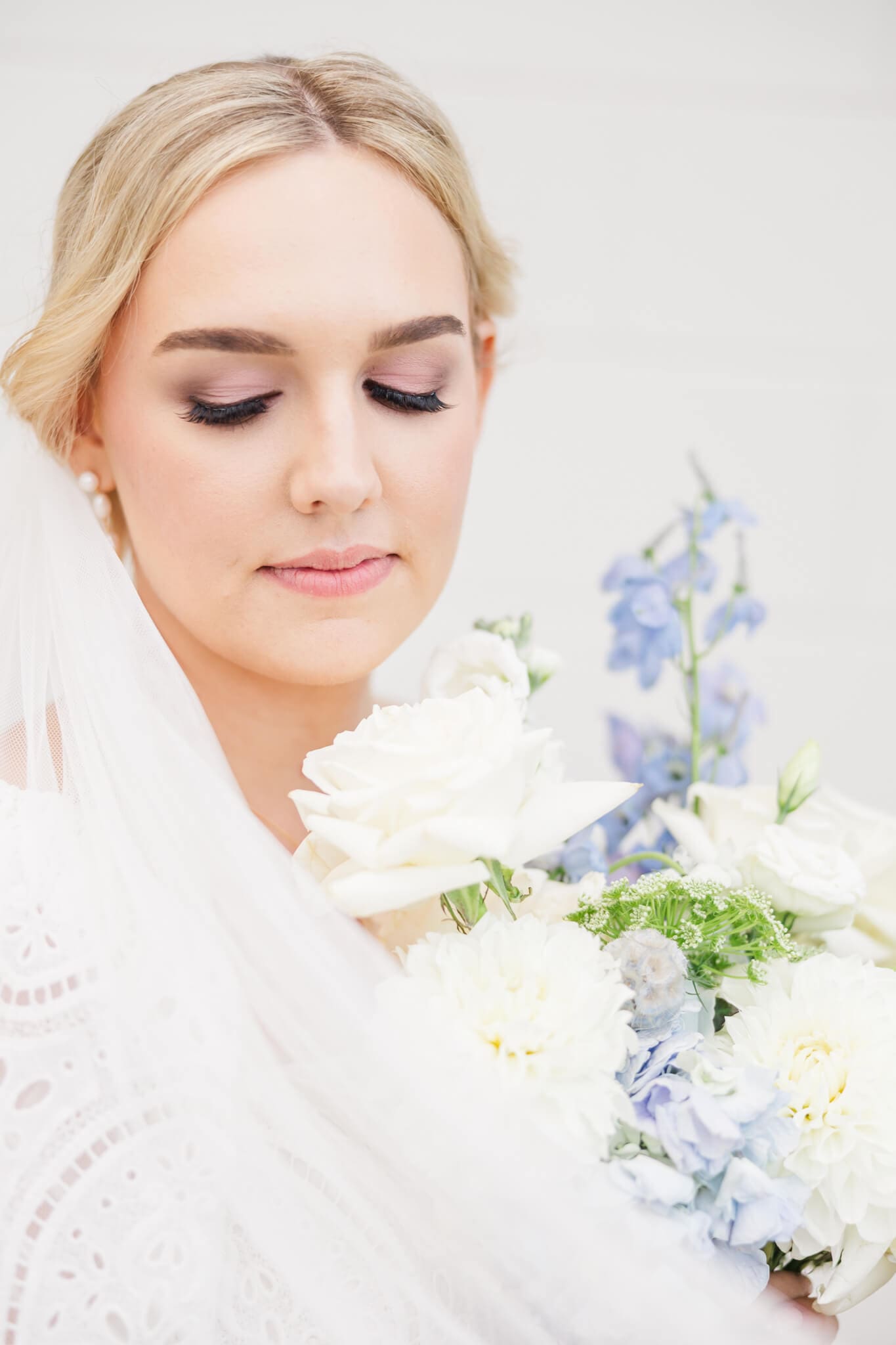 Bride holds her bouquet up close to her face as she looks down at them.