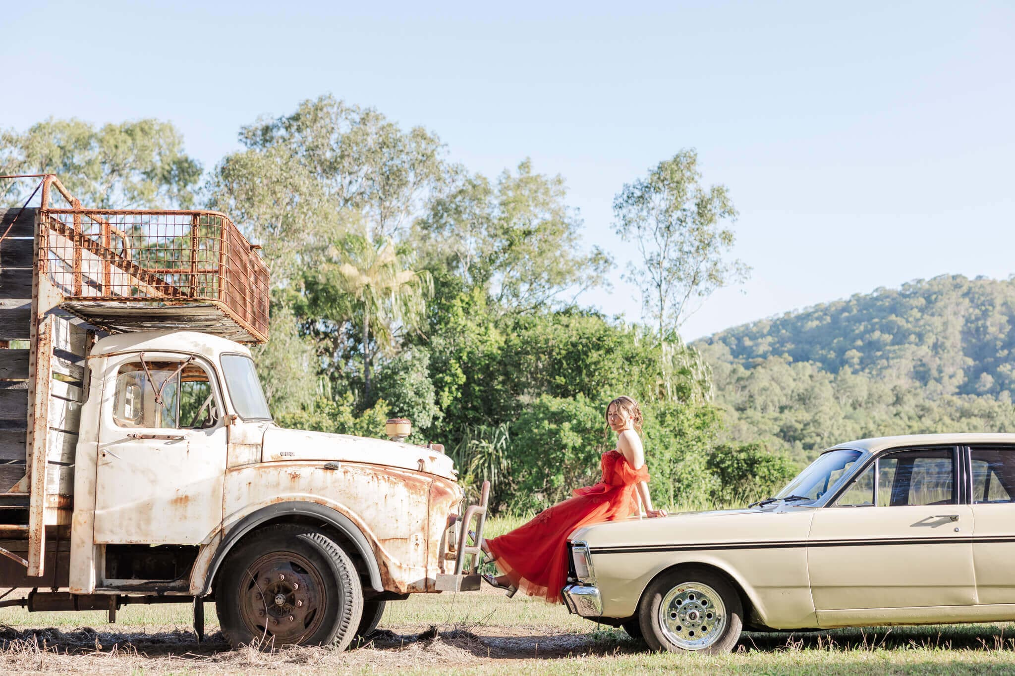 Formal graduate posing between a car and a truck for her Yeppoon formal photos.