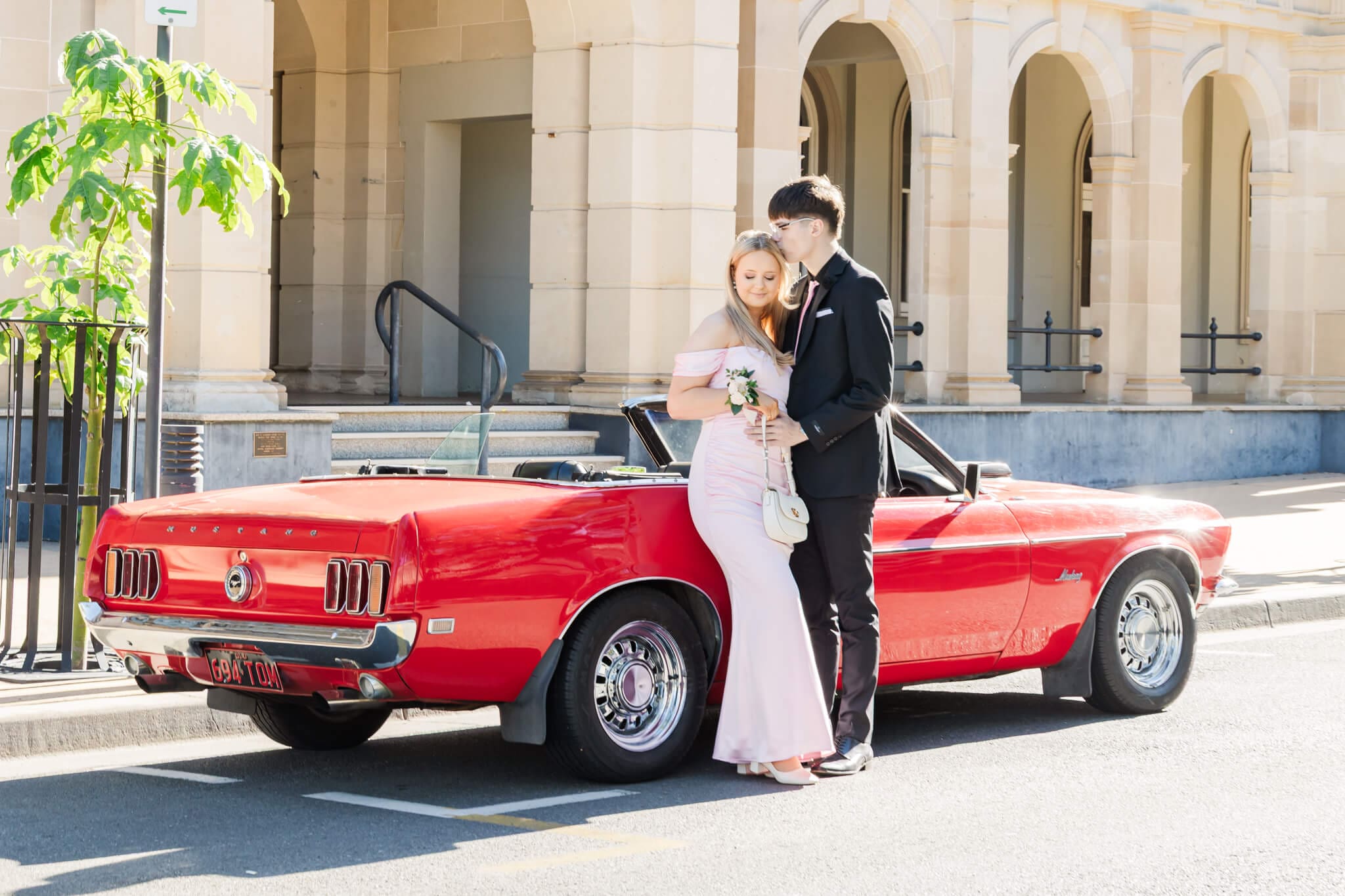 Formal graduates and their red car hire in Rockhampton, posing for their formal photos.