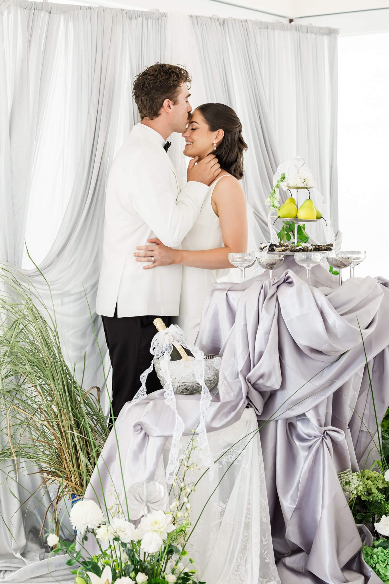 Bride and groom kiss while standing with the cake at a wedding reception. Image by Julie-Anne Photography.