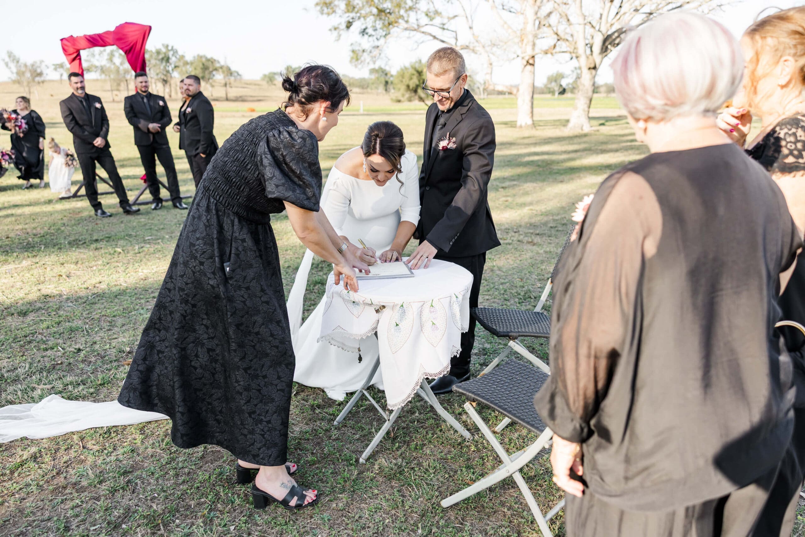 A marriage celebrant assists a couple with signing the register at a wedding in a country Rockhampton wedding venue.