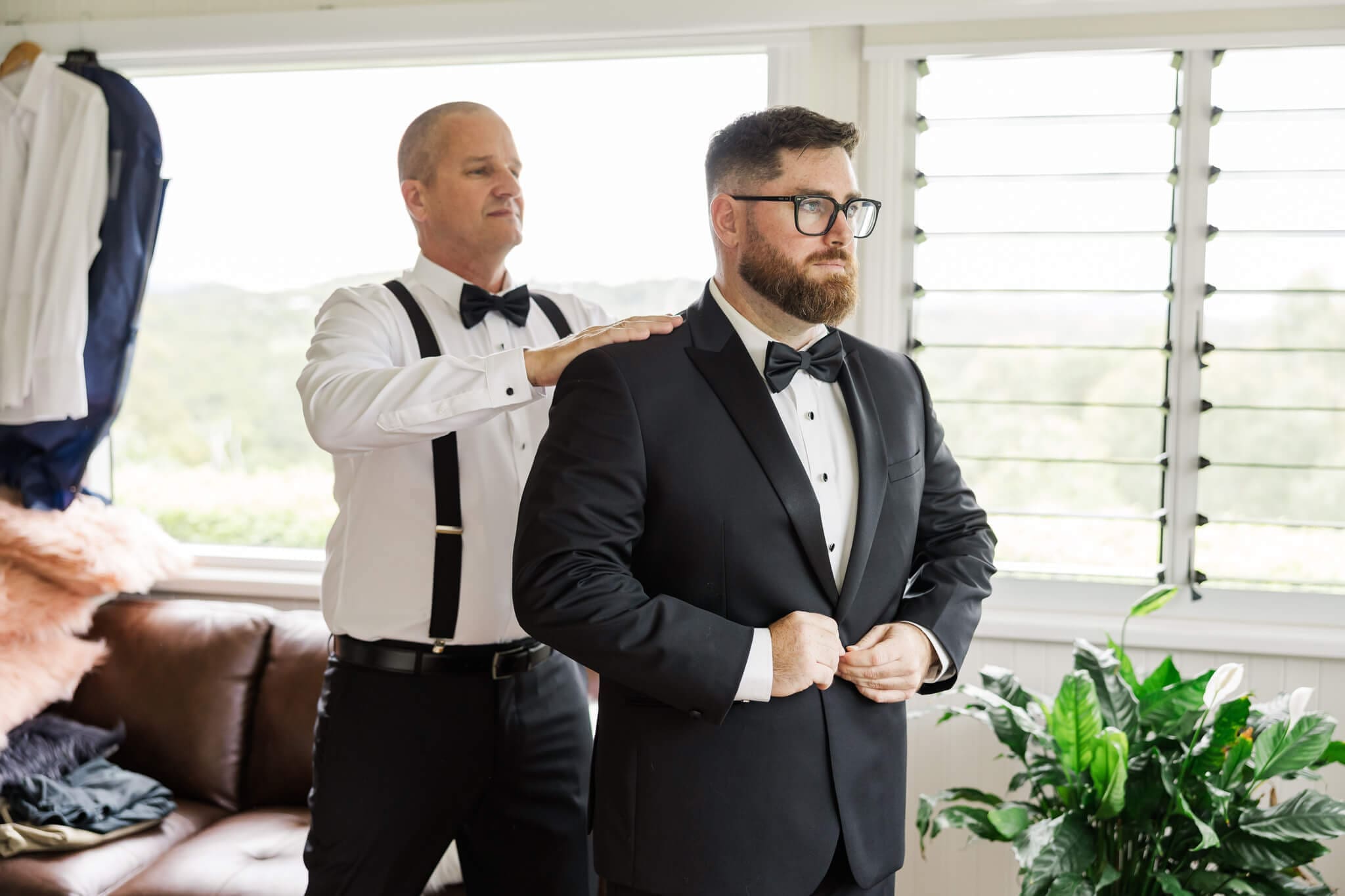 Groom gets dressed into his Rockhampton suit while his best man brushes his shoulders off.