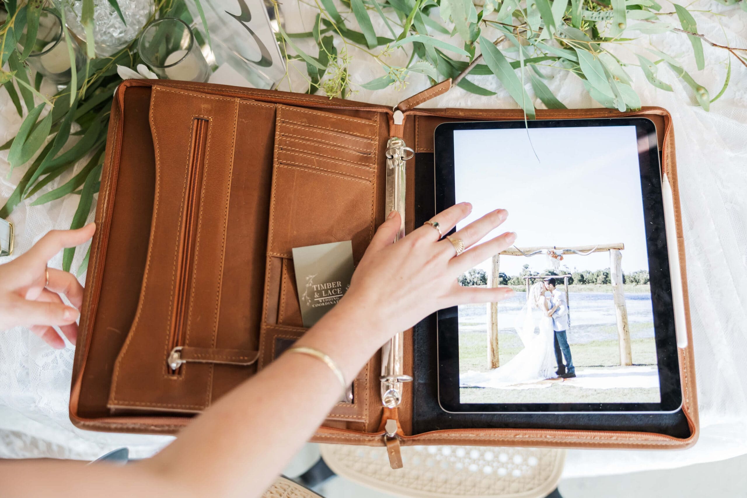 A hand reaching across a wedding planner's folder, with a picture of a bride and groom on an iPad screen.