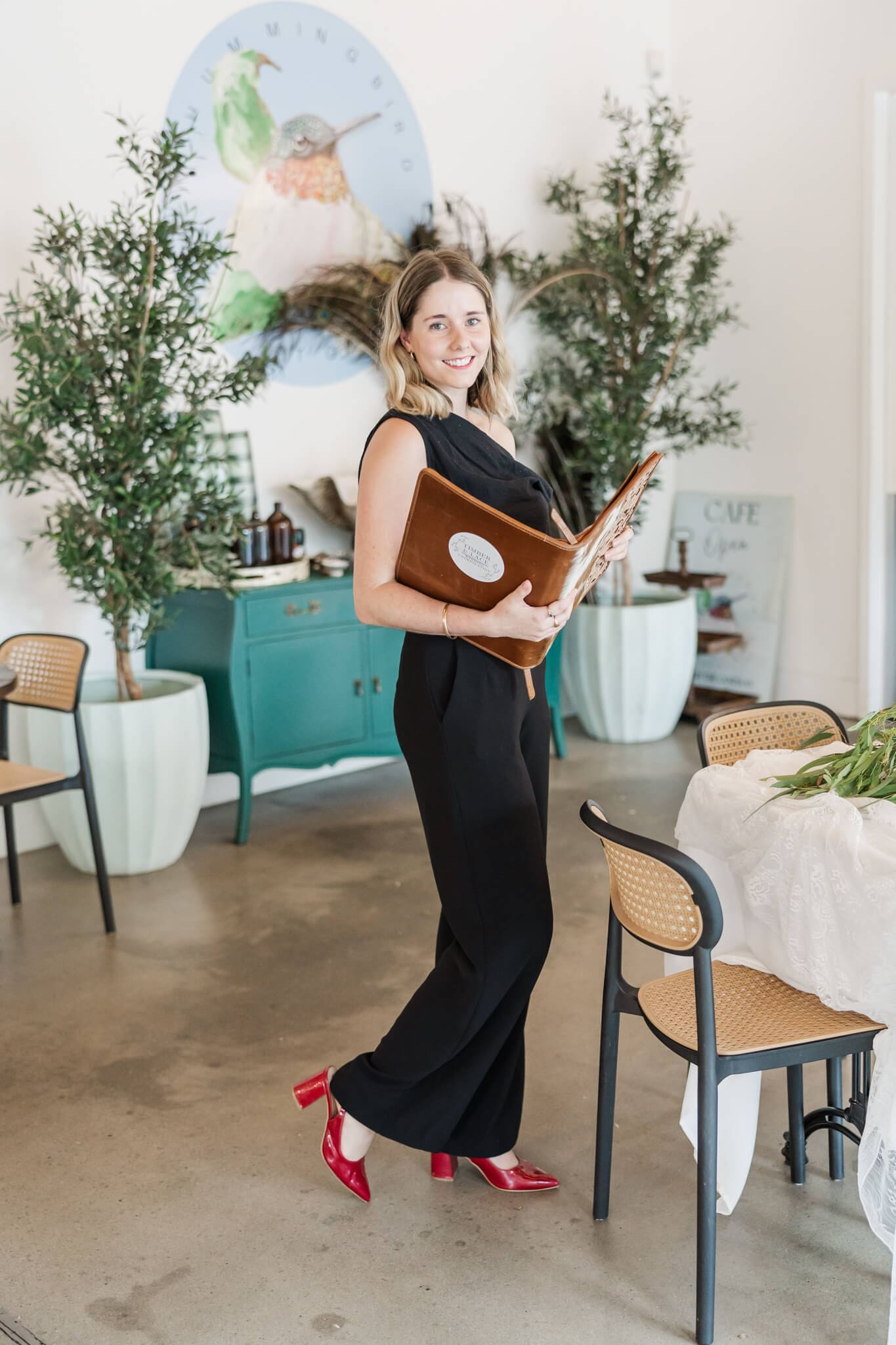 Timber and Lace Coordination owner, Shelby, poses for the camera in uniform, showcasing her planner folder and a pair of beautiful red high heels shoes.