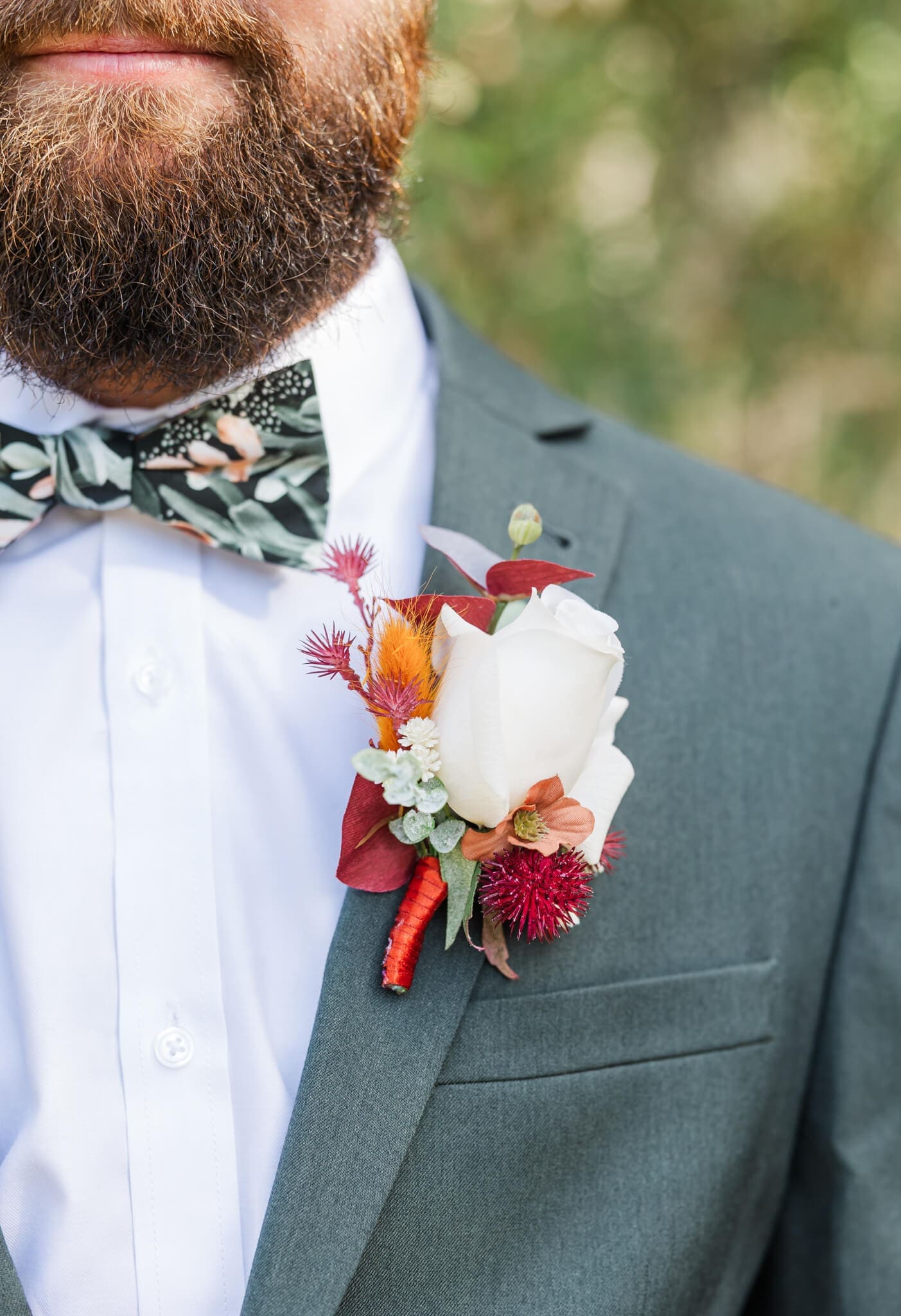 Detail shot of the groom's floral boutonniere, sitting on a earthy green suit jacket.