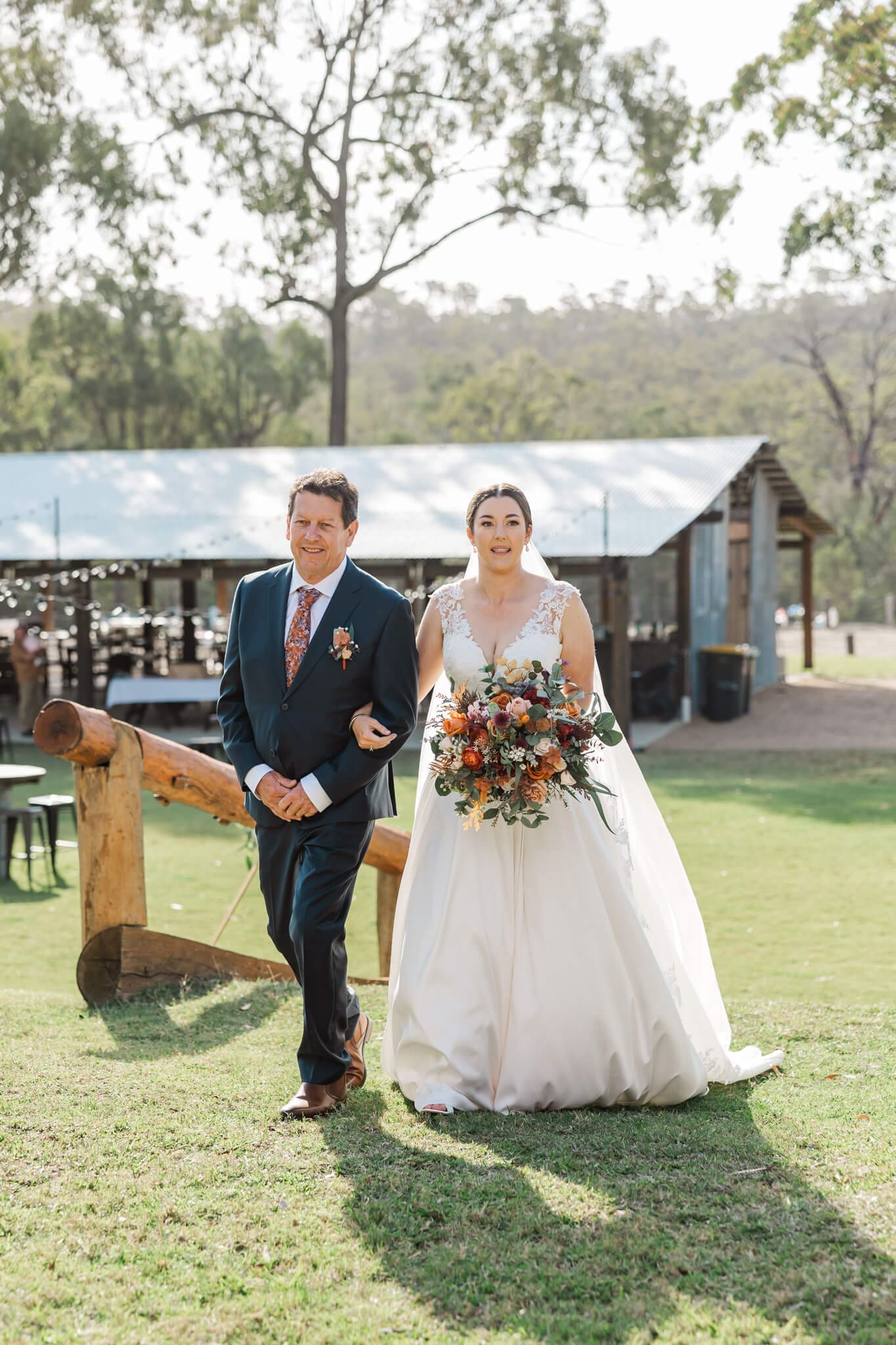Father of the bride walks the bride down the aisle in an outdoor setting.