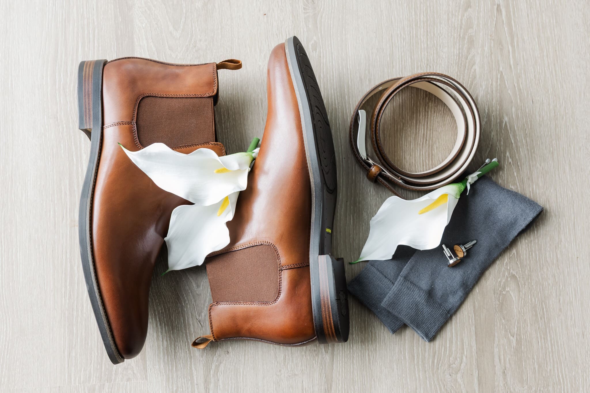 Groom details including brown boots, lily boutonnieres, a belt and cuff links.