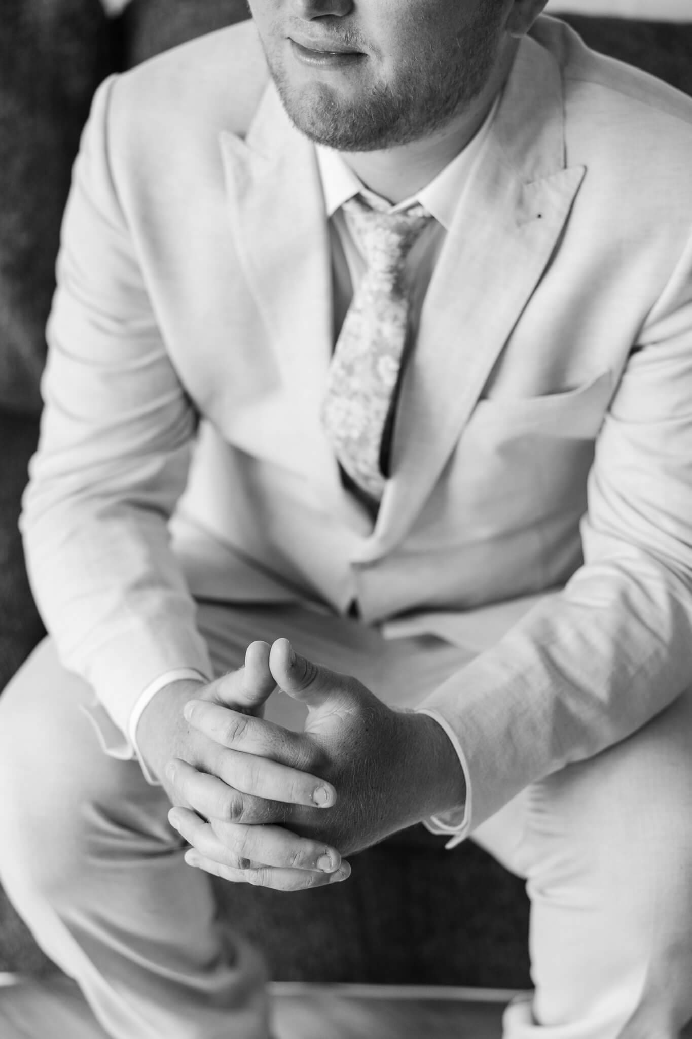 Detail shot of a groom's hands together as he sits looking out the window. Black and white image taken by Julie-Anne Photography.