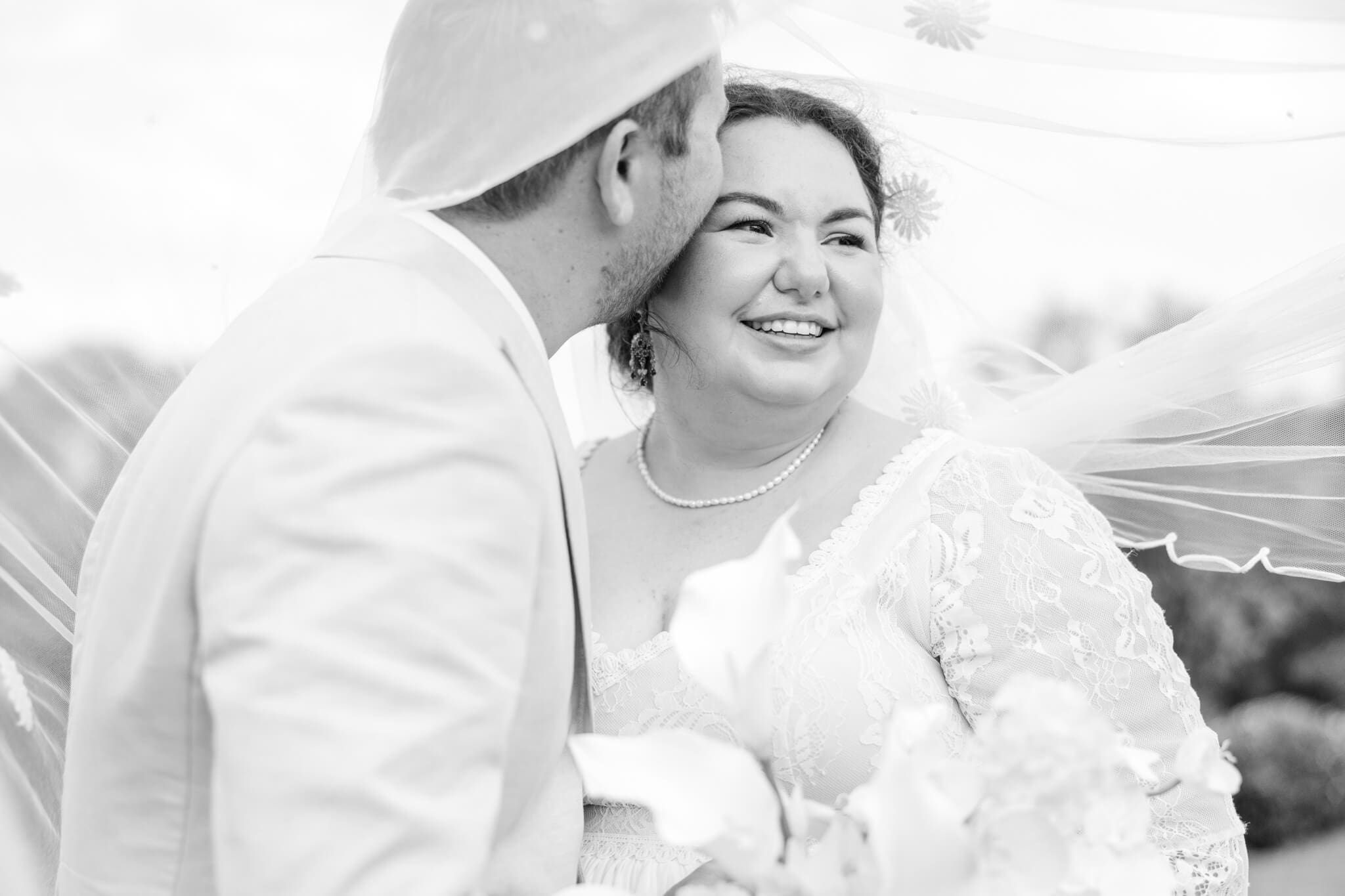 Black and white image of groom kissing the bride under her veil.