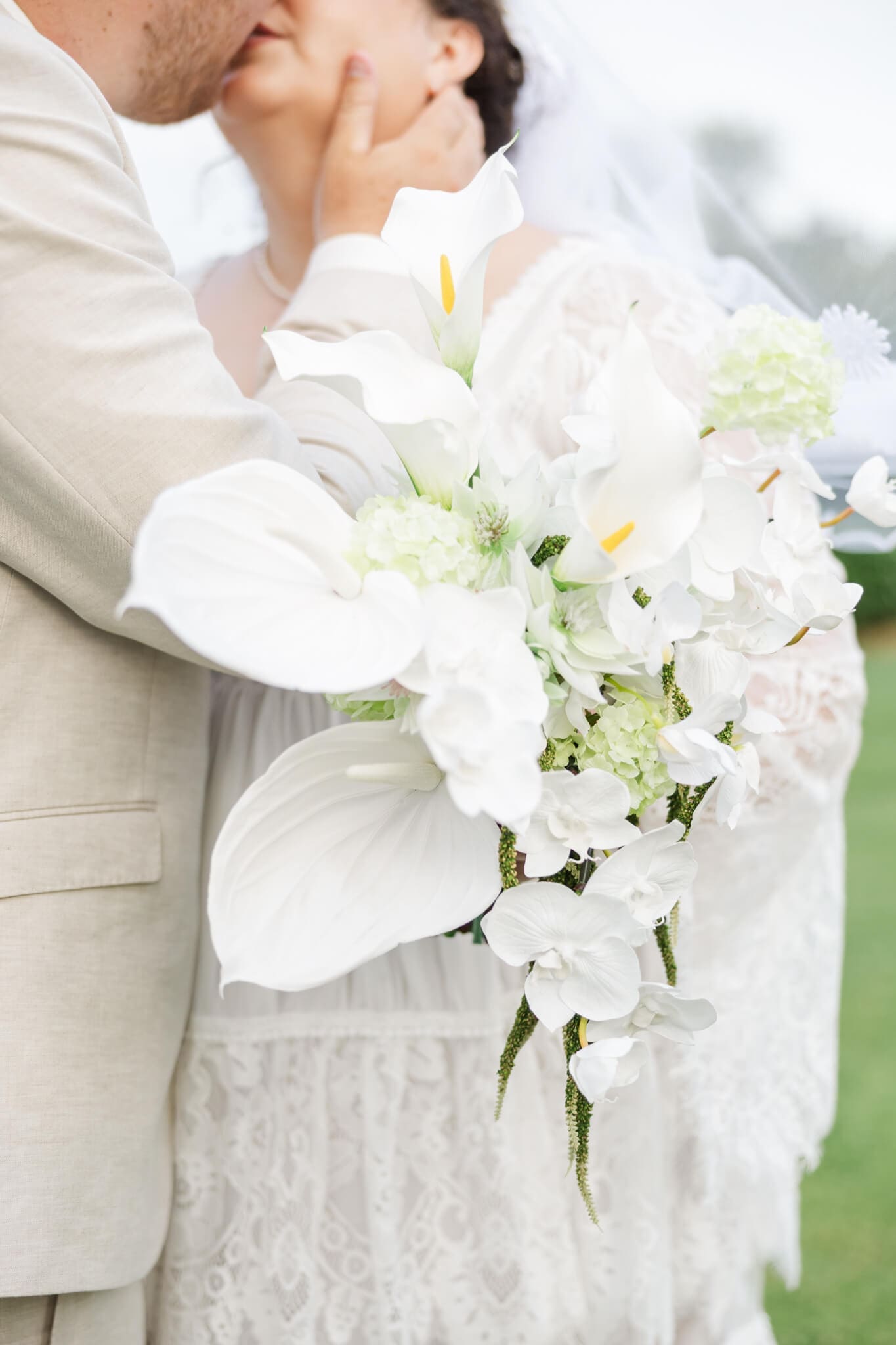 Detail shot of a bride's bouquet with the bride and groom share a kiss in the background.